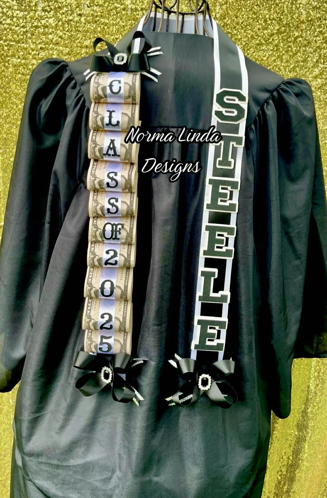 Front facing view of money, layered graduation lei. Featuring Class of 2025 and STEELE in greens, white and black. Adorning are emerald green bows and black gems.