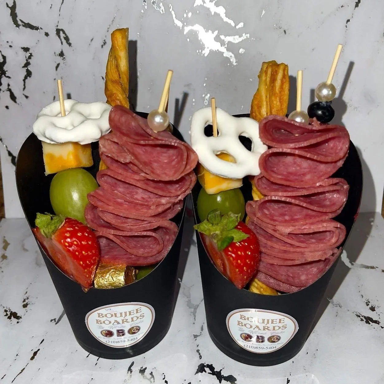 Close up view charcuterie cups featuring seasonal meat, cheese and a garnish featuring strawberry, olive, pretzel and white chocolate