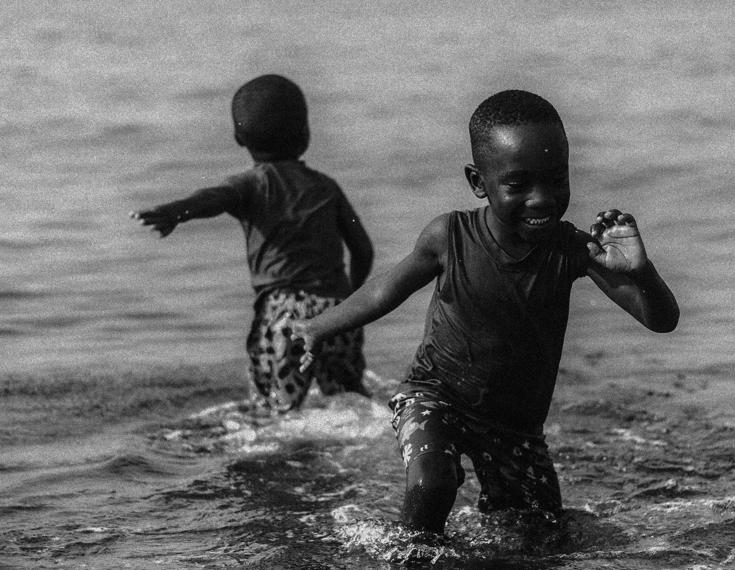 Two young boys playing and running in shallow water at the beach, smiling and enjoying their time, Photographed by Ussi'n Yala in Port-Gentil, Gabon, 2016