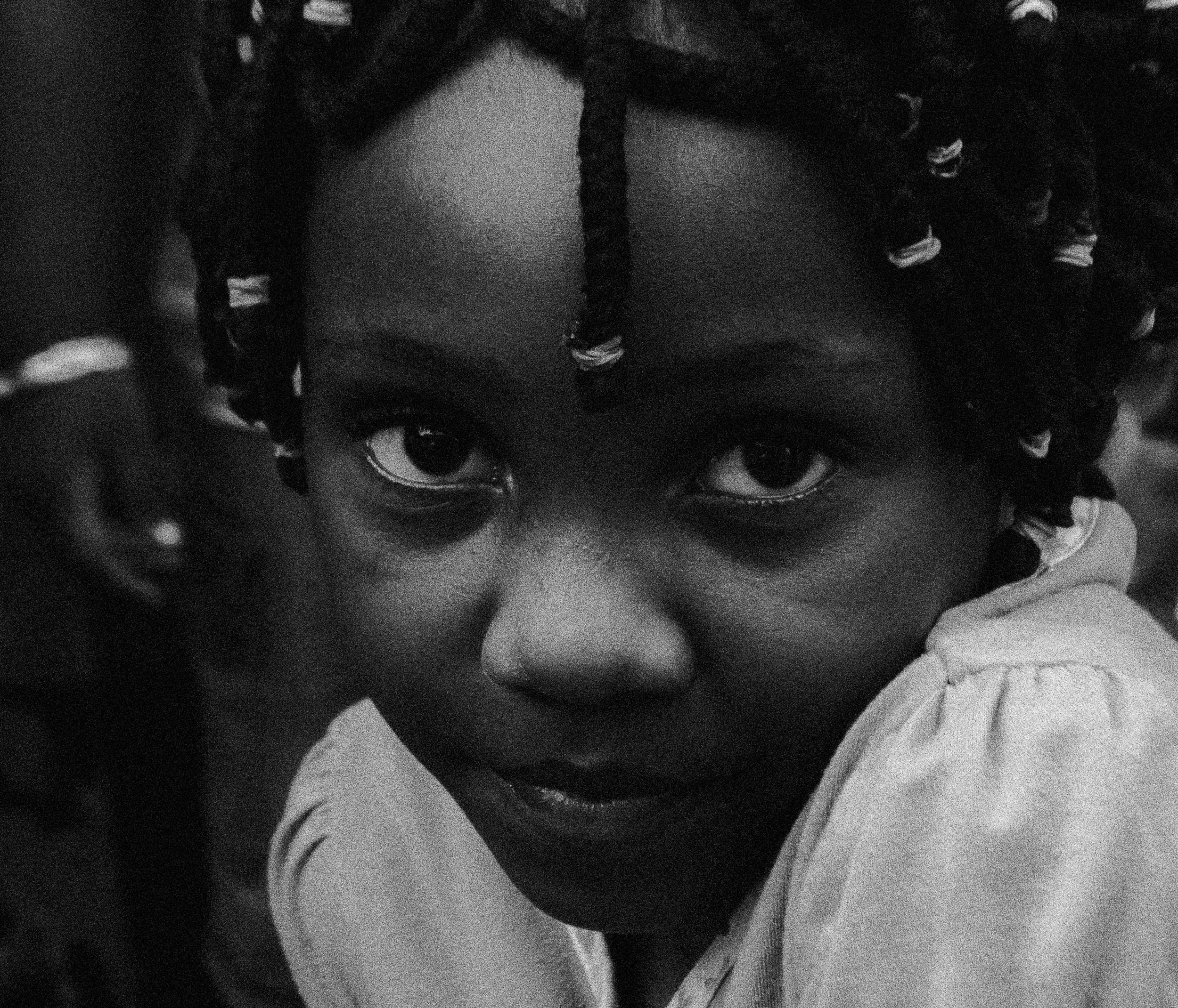Close-up black and white photograph of a woman with braided hair, looking directly at the camera, Photographed by Ussi'n Yala in Libreville, Gabon, 2016