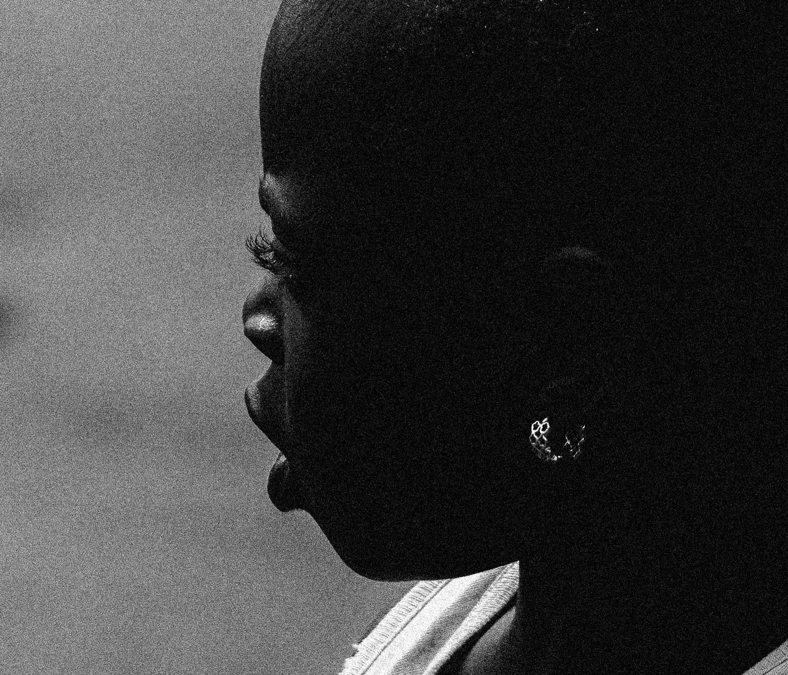 A black-and-white close-up profile of a person with earrings and short hair, with the face partially in shadow, Photographed by Ussi'n Yala in Gamba, Gabon, 2016