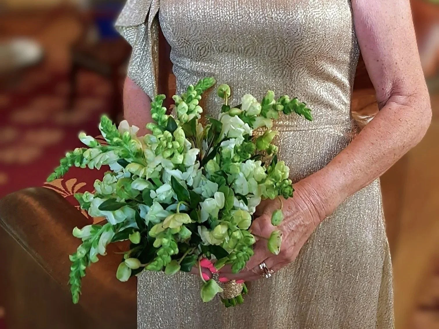 A person holding a small bouquet of light green and white flowers, wearing a shimmery gold dress.