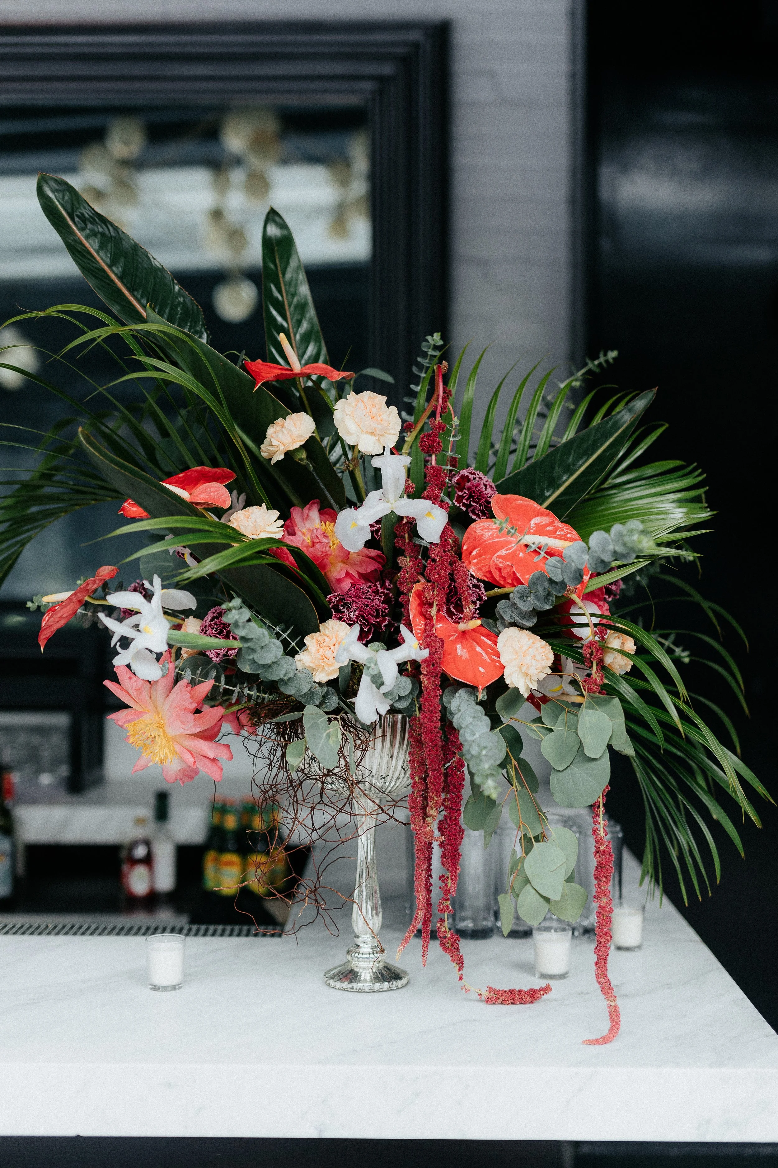 Elegant floral arrangement with pink, white, and red flowers and lush green leaves in a crystal vase on a white marble table.