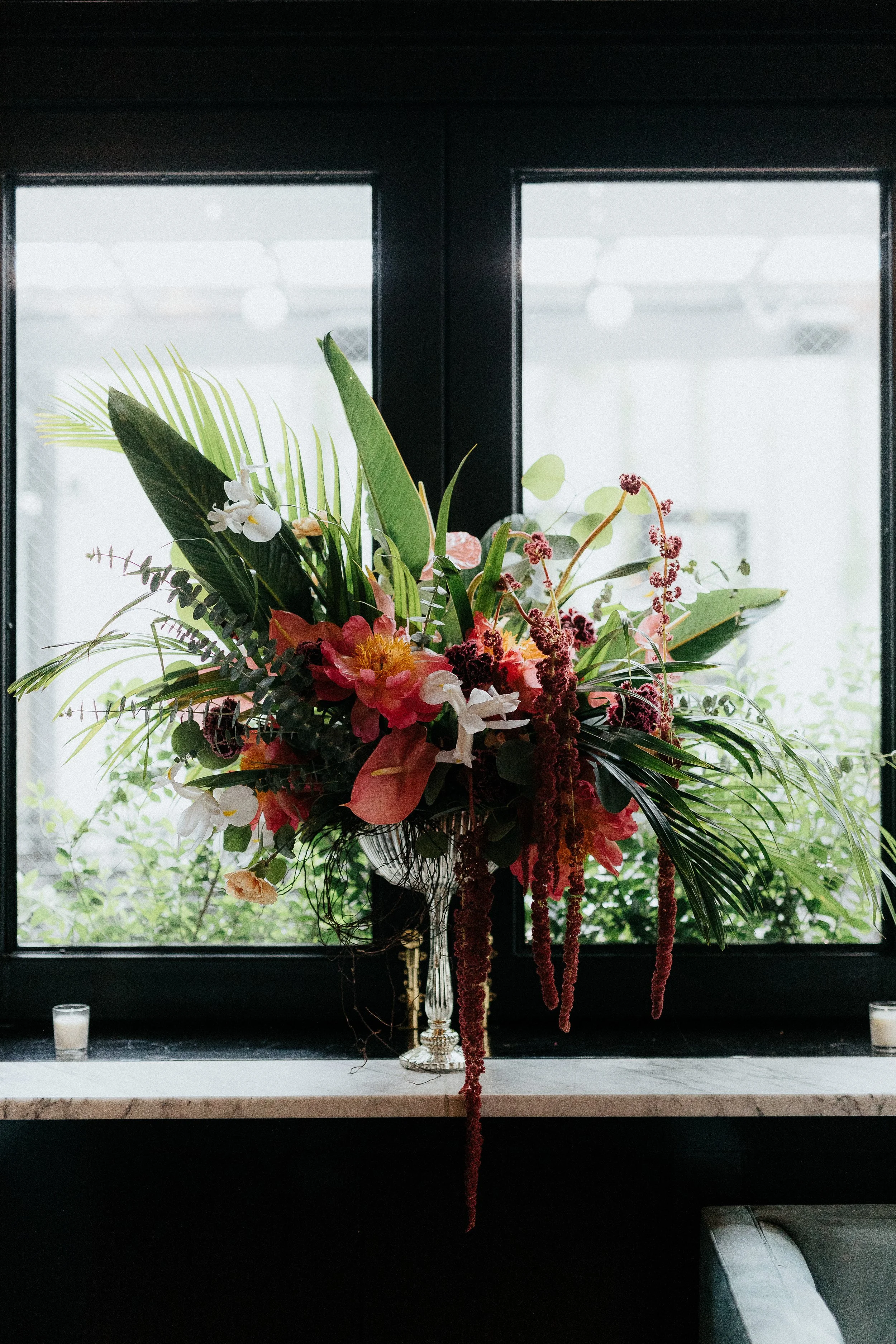 A colorful flower bouquet placed on a windowsill with a black window and candles on each side.