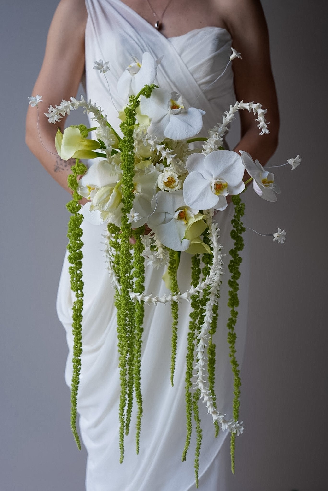 A woman in a white dress holding a cascading bouquet of white orchids and green foliage.