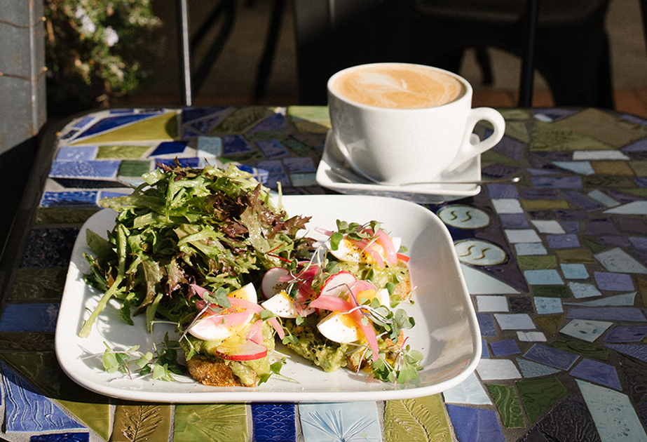 Salad with mixed greens and topped with microgreens, served with a side of leafy greens, paired with a cup of coffee or latte