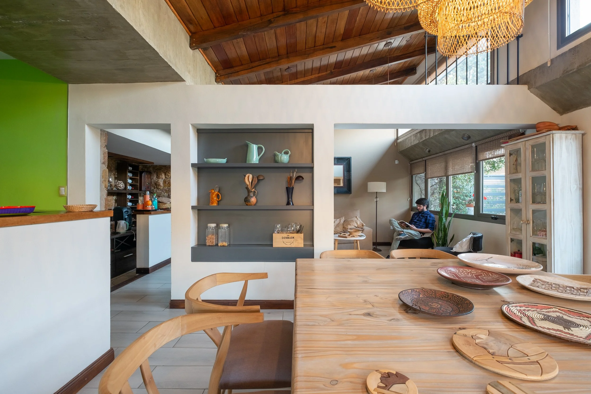 Amplio espacio de estar y comedor de concepto abierto, con cielorraso de madera, una gran mesa de comedor también de madera con platos decorativos, casa en Alta Gracia, Córdoba.