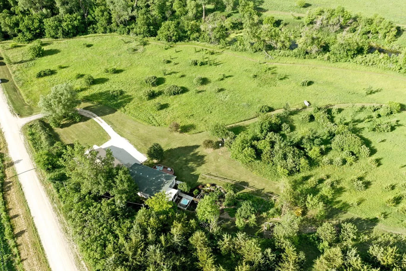 Aerial view of a green house surrounded by trees and open grassy fields.