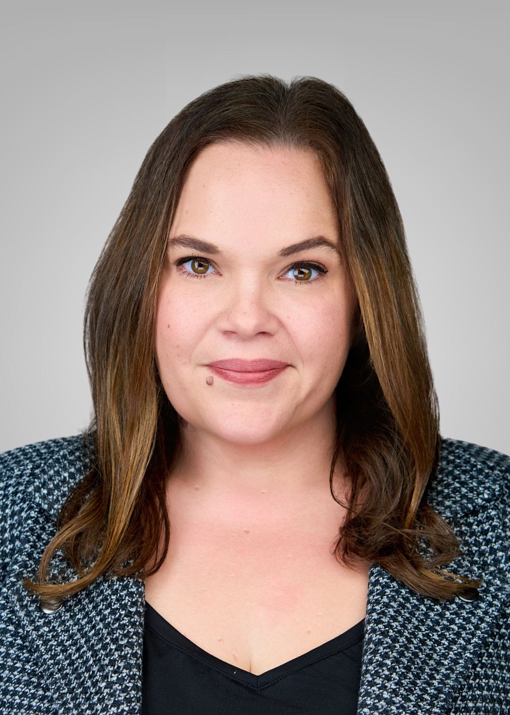 Headshot of a woman with shoulder-length brown hair, wearing a black top and patterned blazer, against a light gray background.