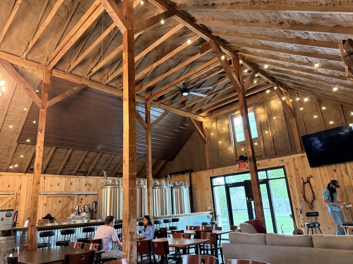 Interior of a rustic wooden brewery with high ceilings, string lights, and seating for patrons.