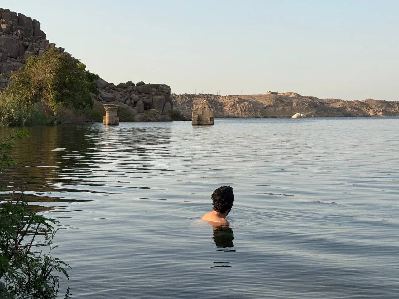 Persona nadando en el Nilo con templos detrás.