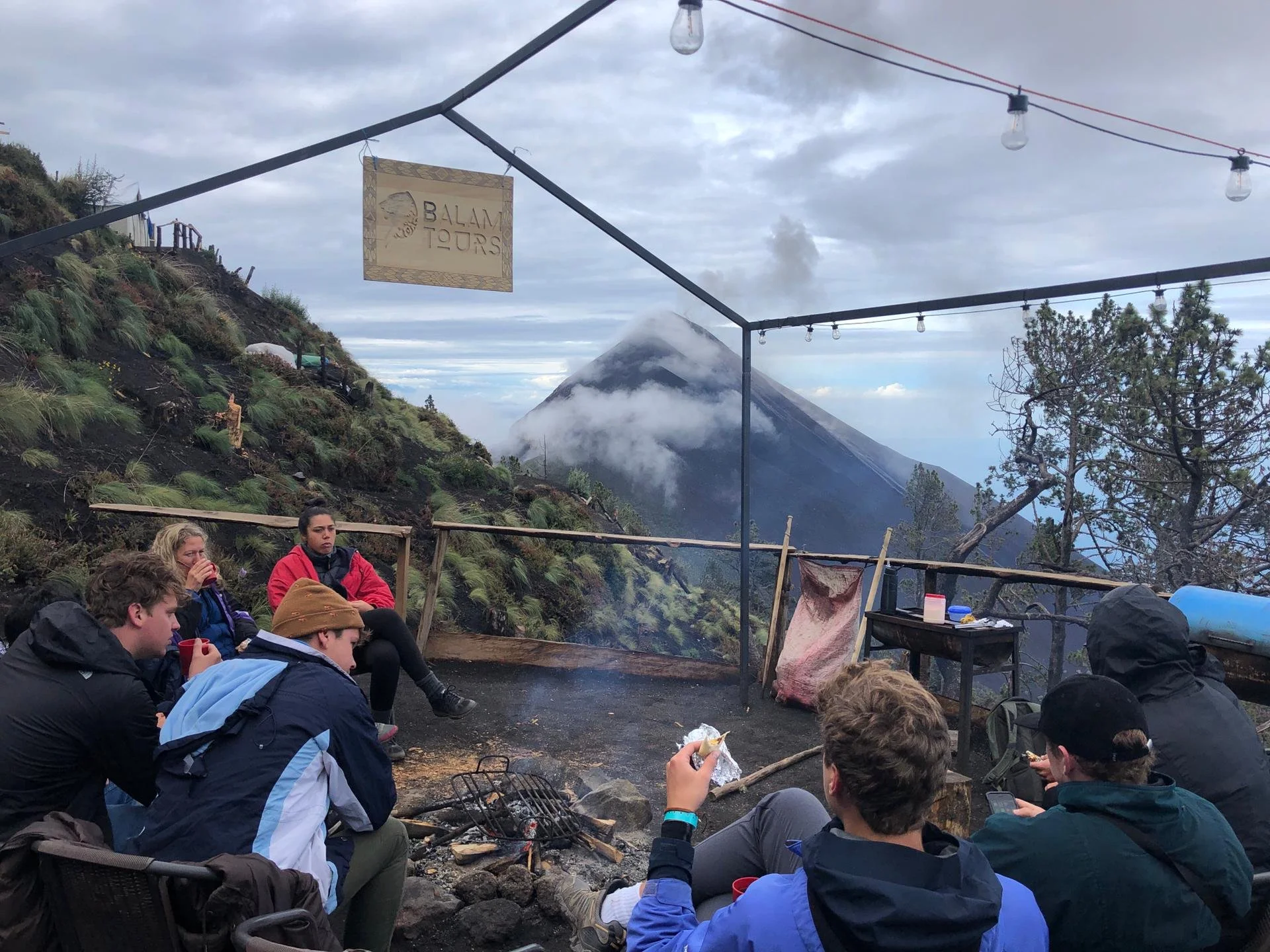Personas alrededor de una fogata con el volcán Fuego al fondo