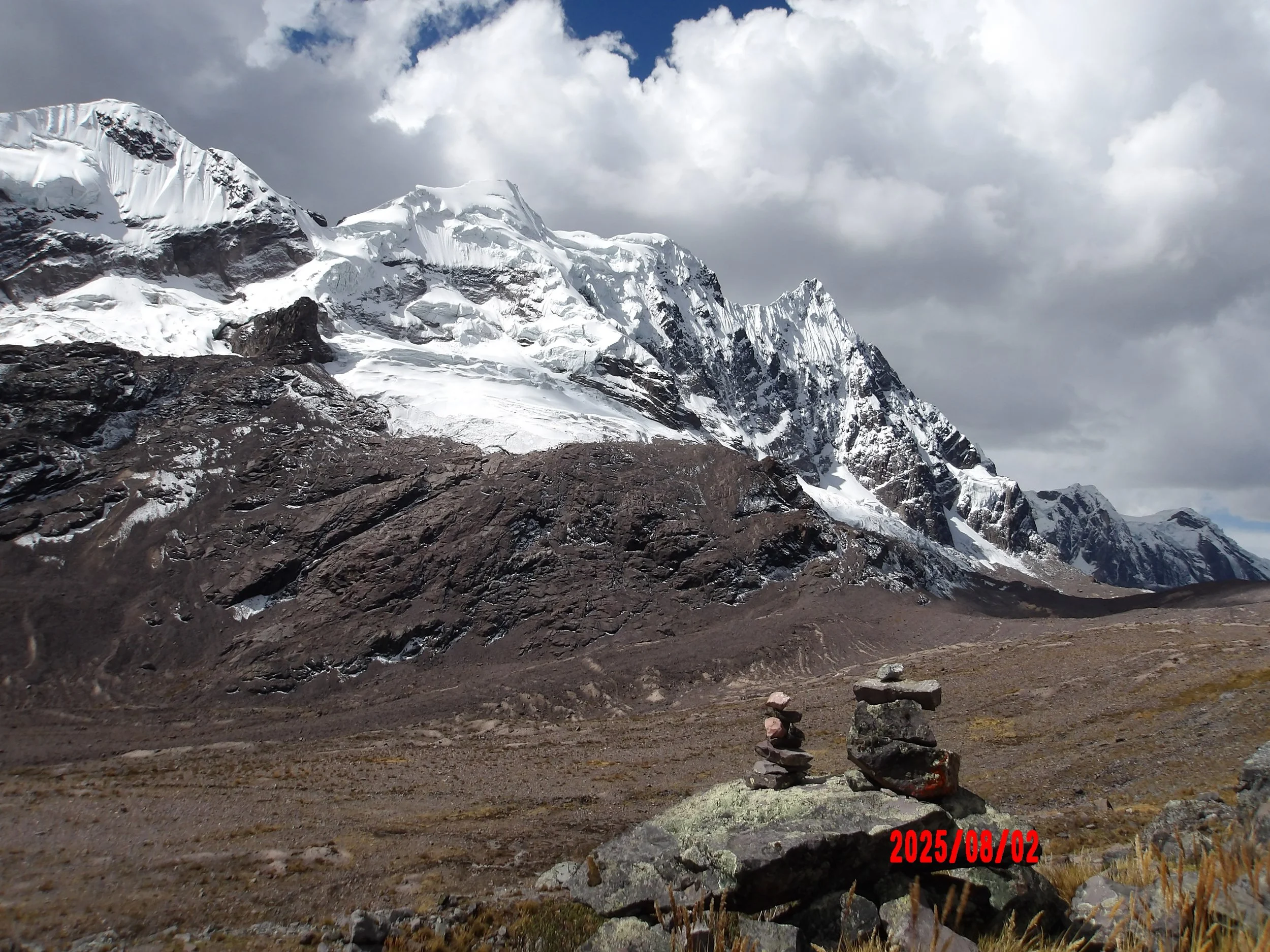 Apachetas sobre una piedra con montaña con glaciares al fondo en el trek de Ausangate