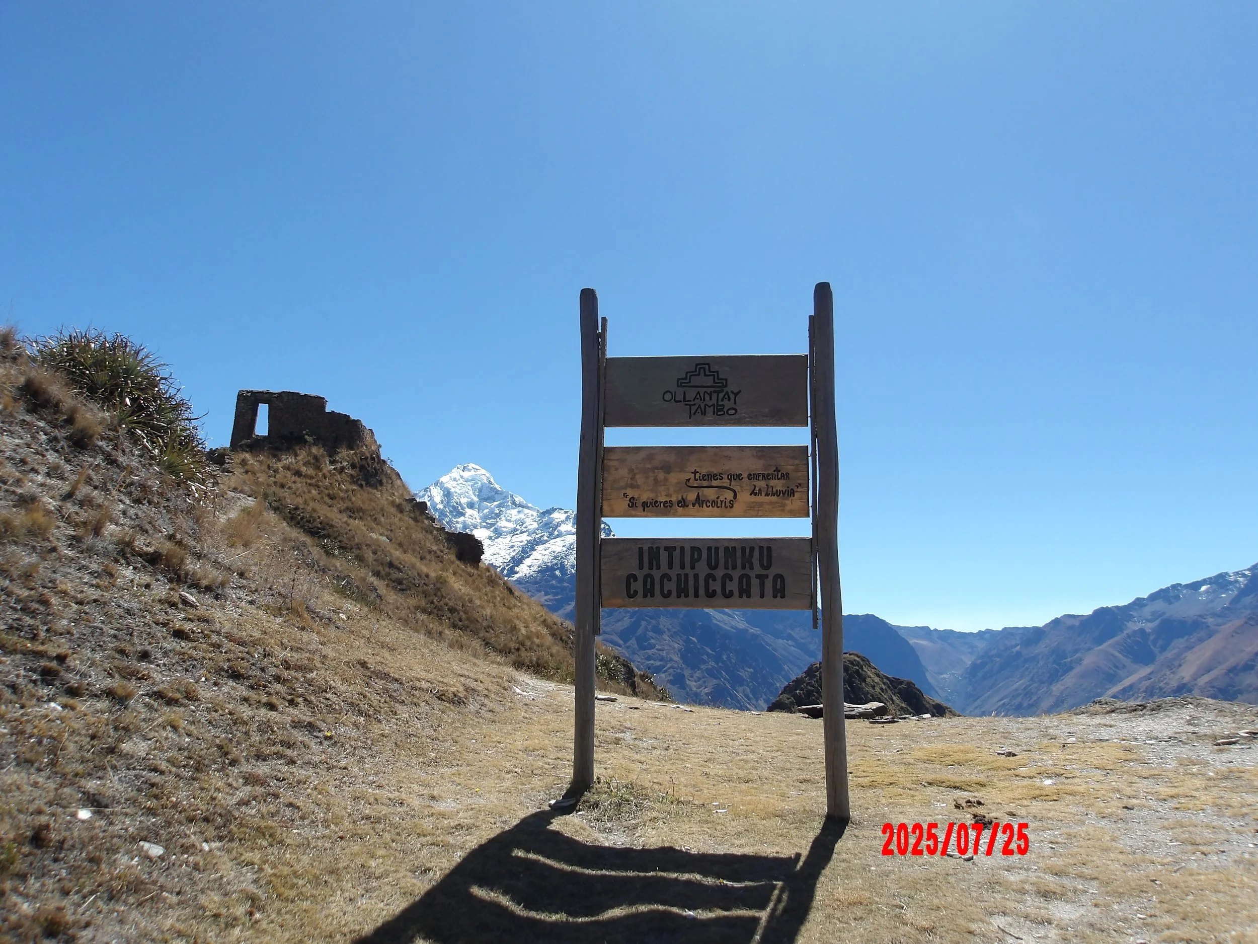 Letrero de ruinas de Inti Punku con montañas nevadas al fondo.