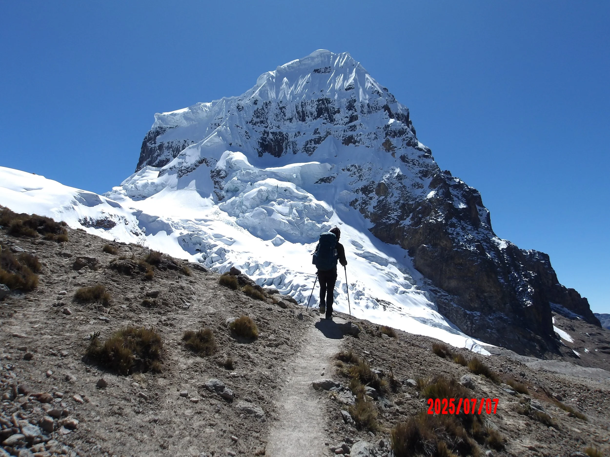 Sendero y persona caminando con un pico nevado al fondo, en la cordillera de Huayhuash.