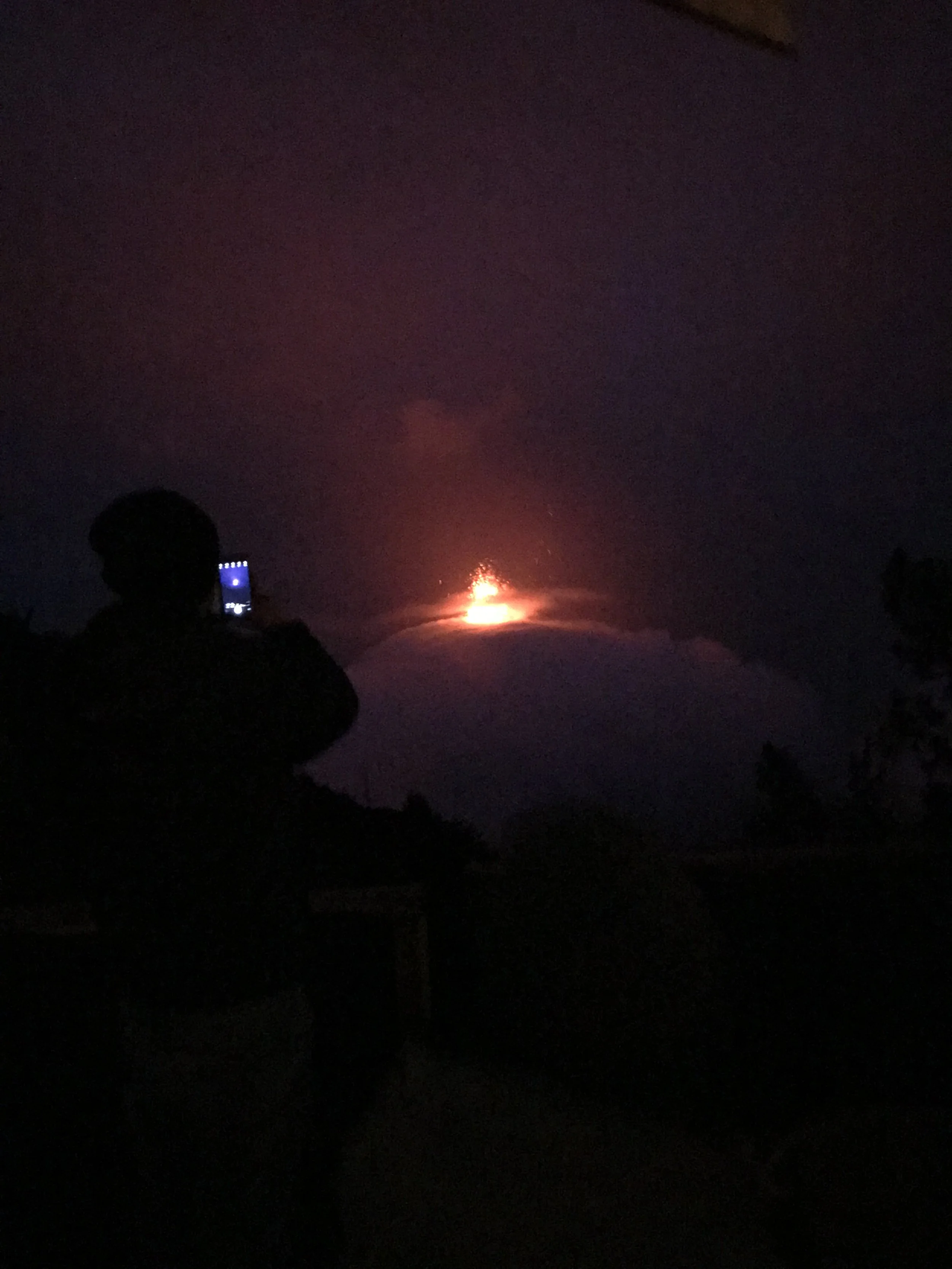 Foto nocturna de la erupción del Volcán Fuego con persona en su celular.