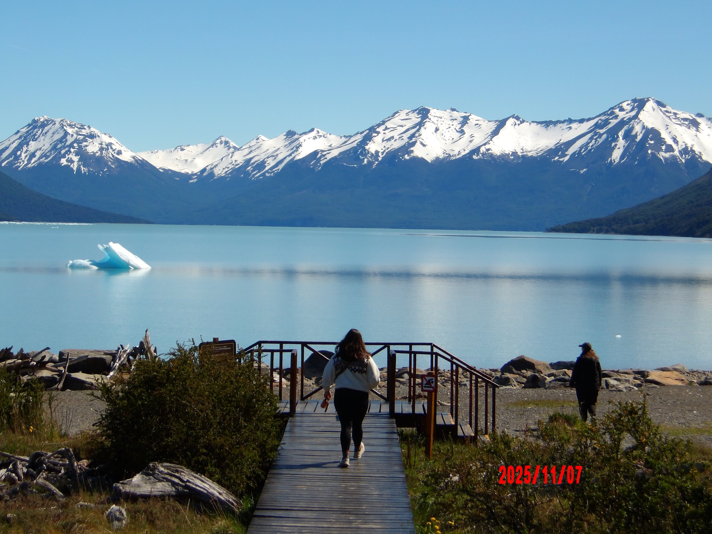 Mujer caminando con lago al fondo y montañas nevadas, en Patagonia, Argentina.