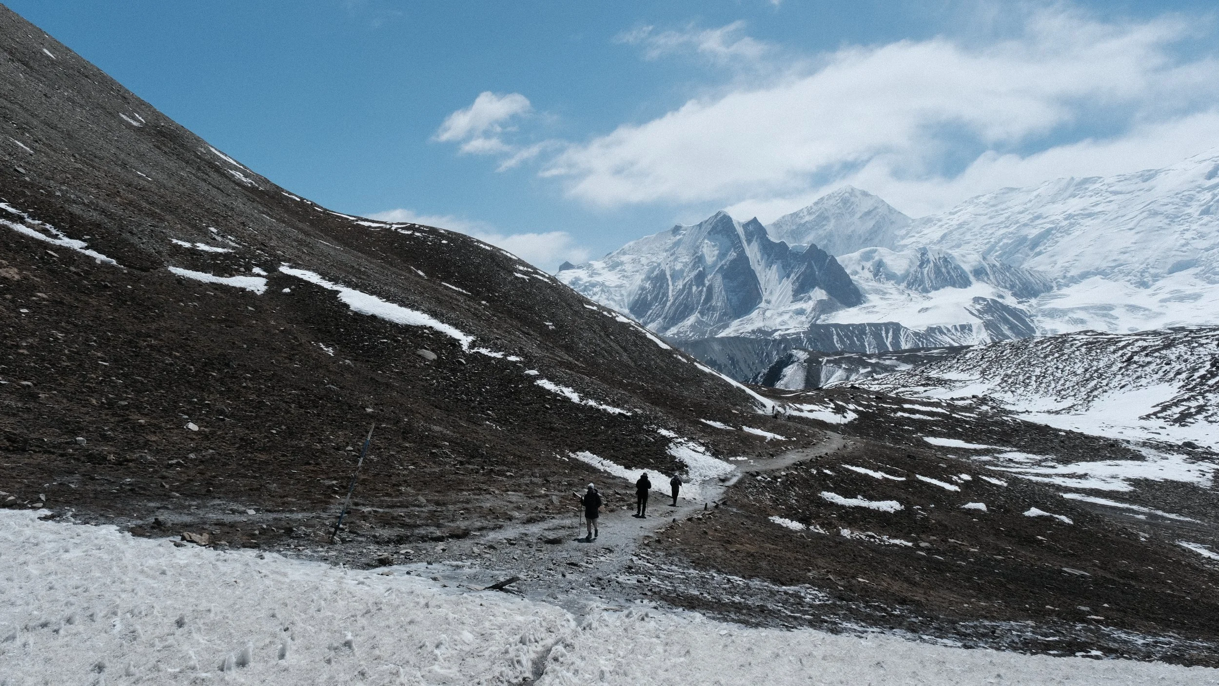 Sendero con nieve y personas caminando con montañas nevadas al fondo. En Nepal.