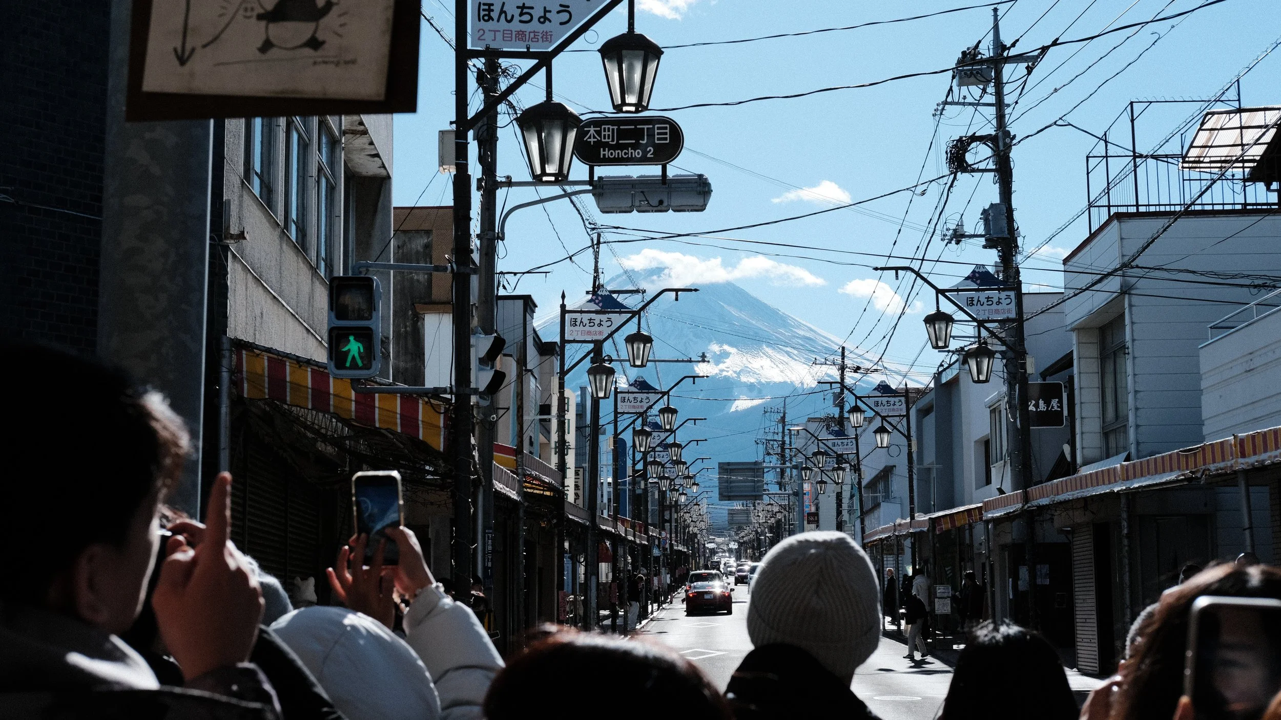 Personas en una calle japonesa tomando fotos con el Monte Fuji al fondo.