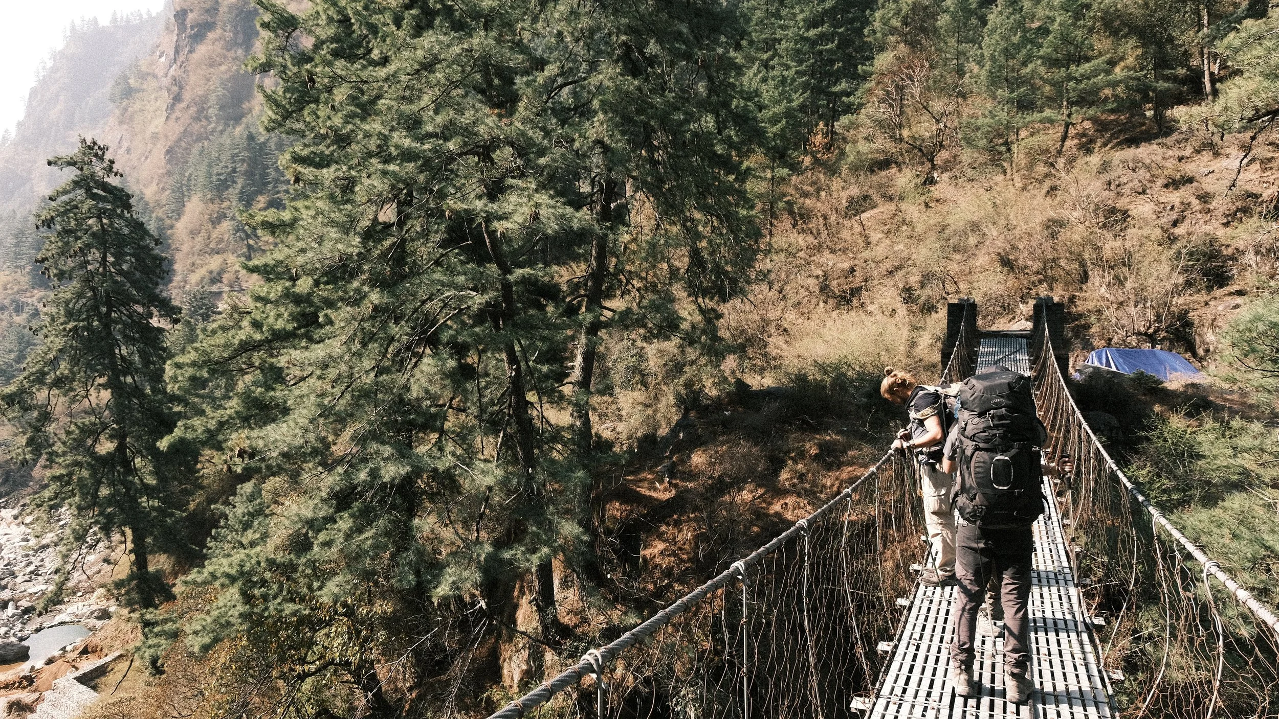Personas cruzando un puente colgante en el Circuito de Annapurna