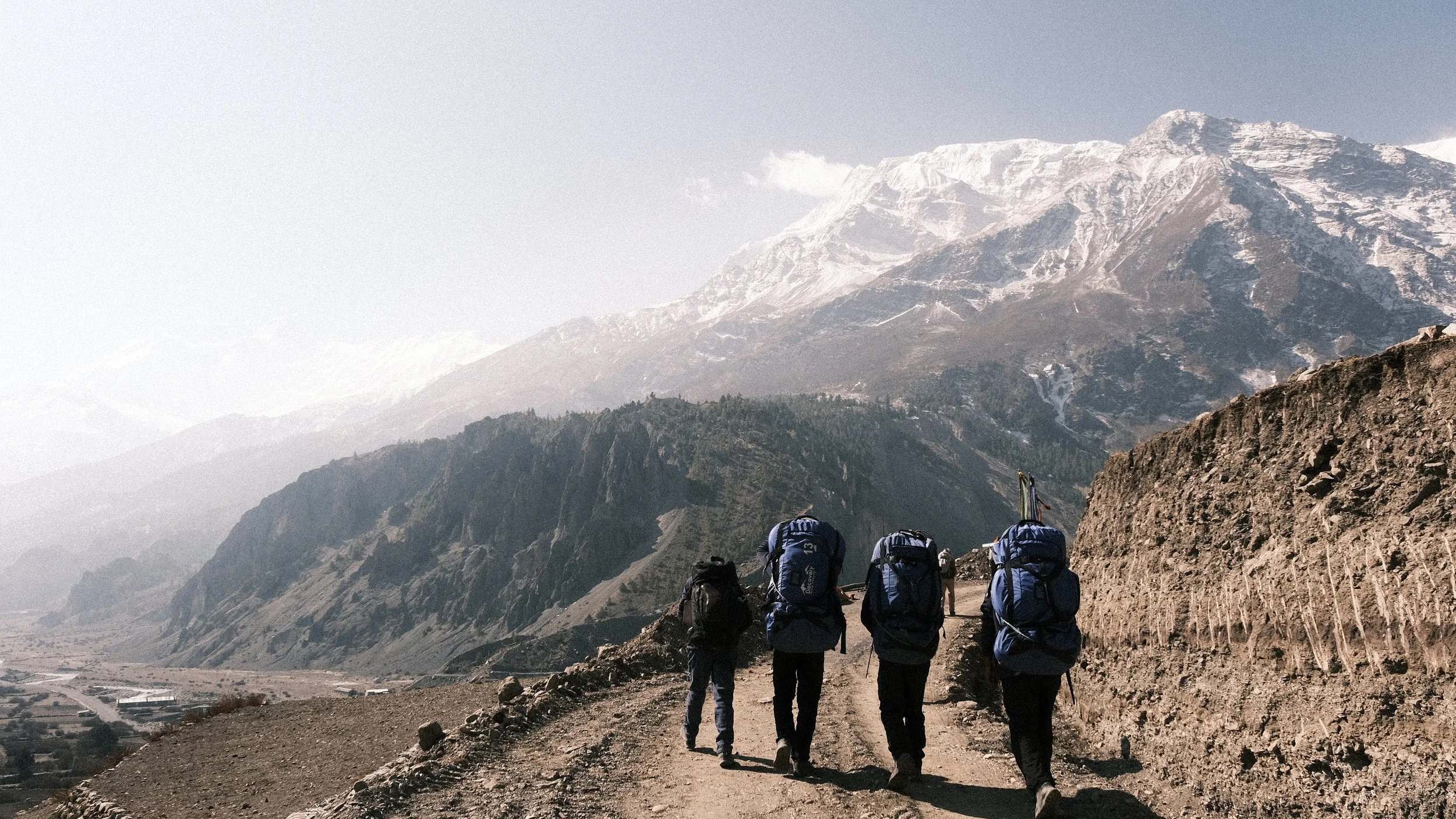 Personas caminando en Nepal con montañas nevadas al fondo.