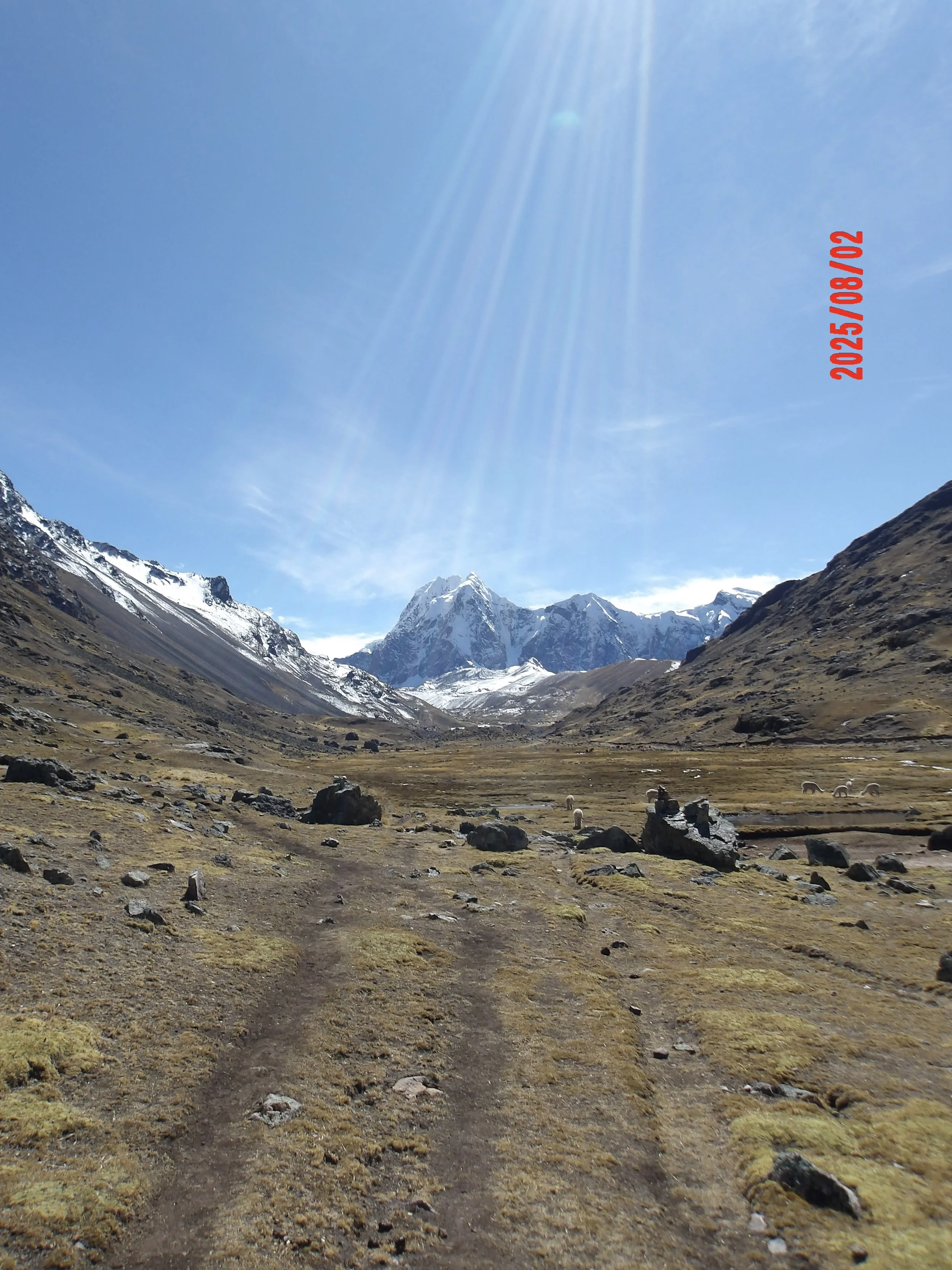 Sendero en el trek de Ausangate con montaña nevada al fondo y los rayos del sol cayendo