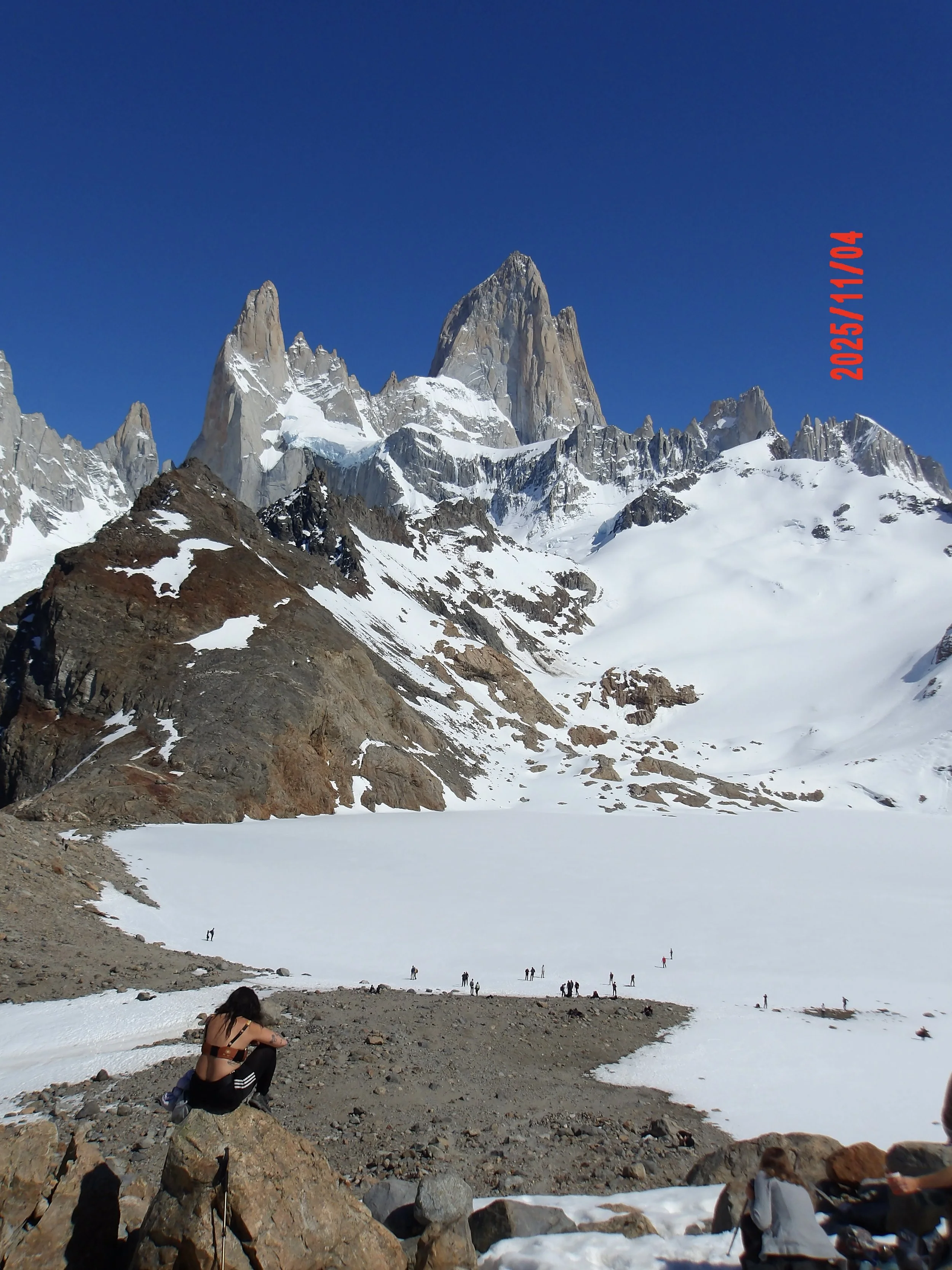 Mujer sobre una piedra con el Fitz Roy al fondo y la laguna congelada