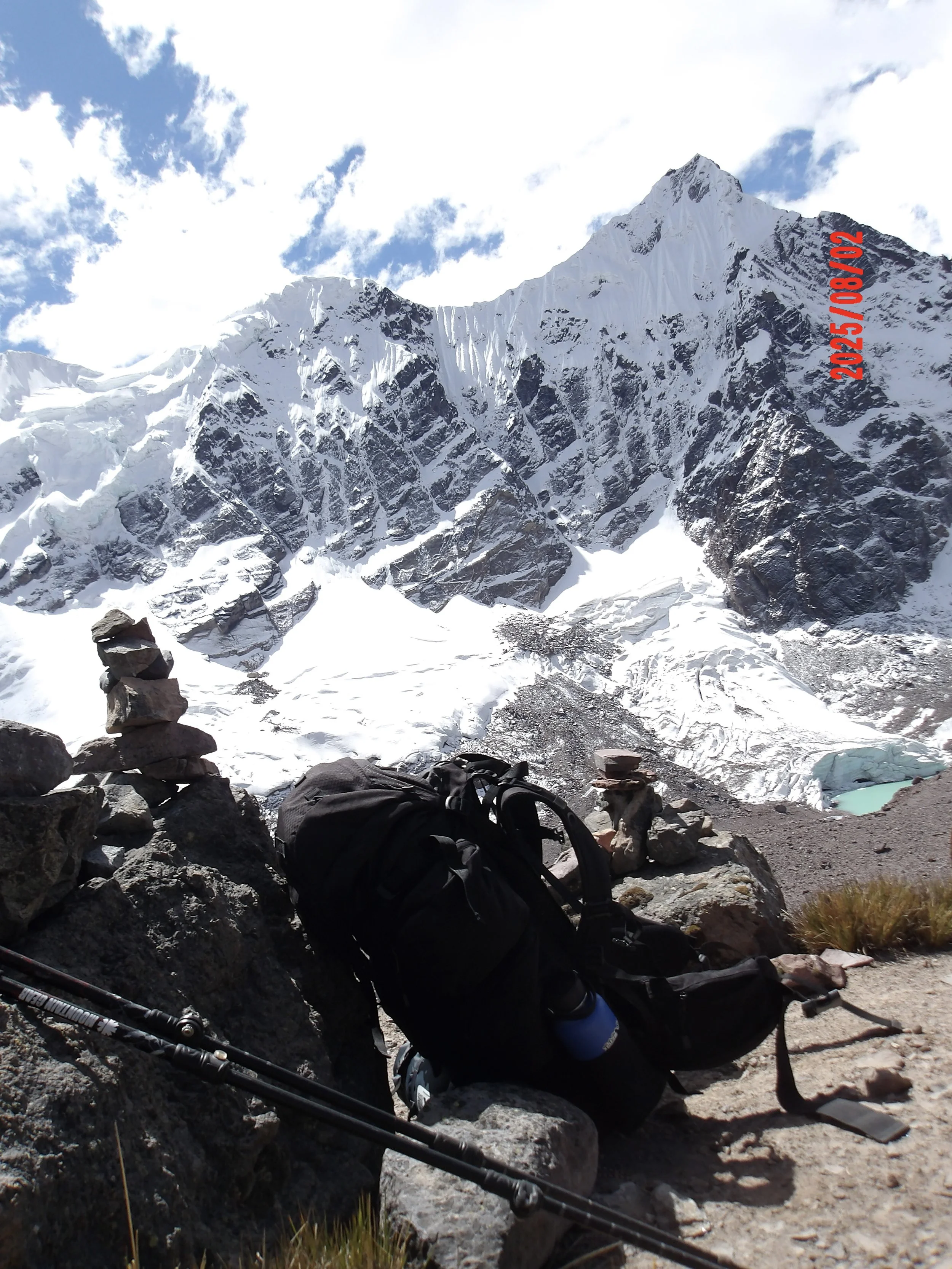 Maleta y bastones de caminata con montañas nevadas al fondo.