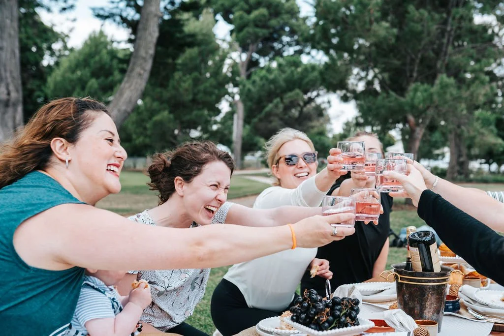 Guests enjoying a luxury picnic experience in Melbourne, raising a toast during a Pilates Picnic celebration surrounded by nature.