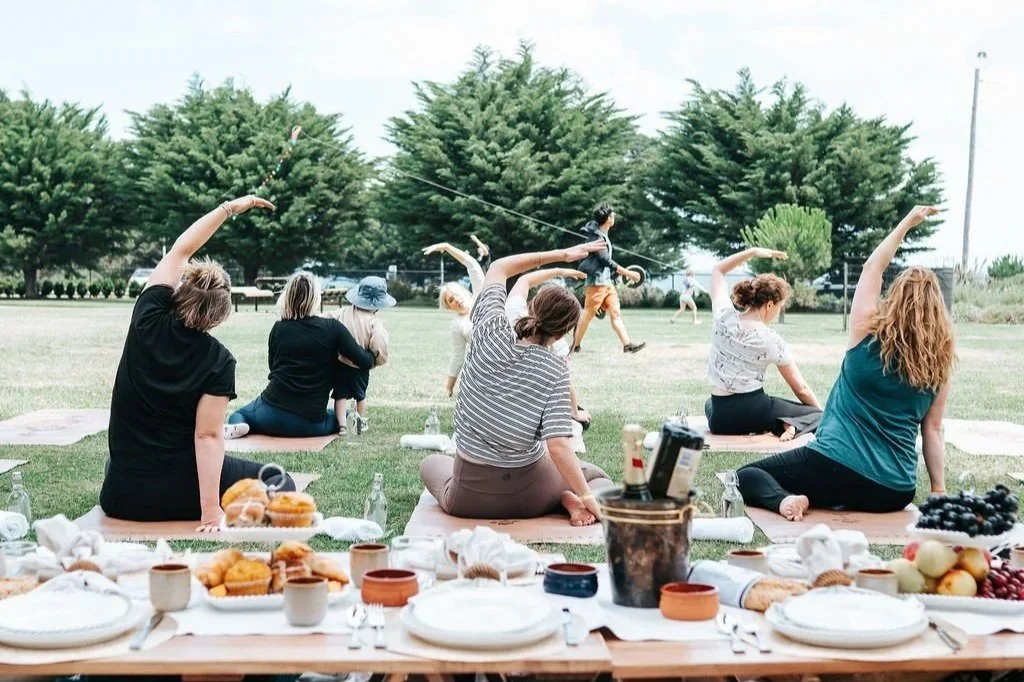 Guests enjoying an outdoor Pilates session in a park setting, with a beautifully styled picnic experience featuring refreshments and luxury tableware.