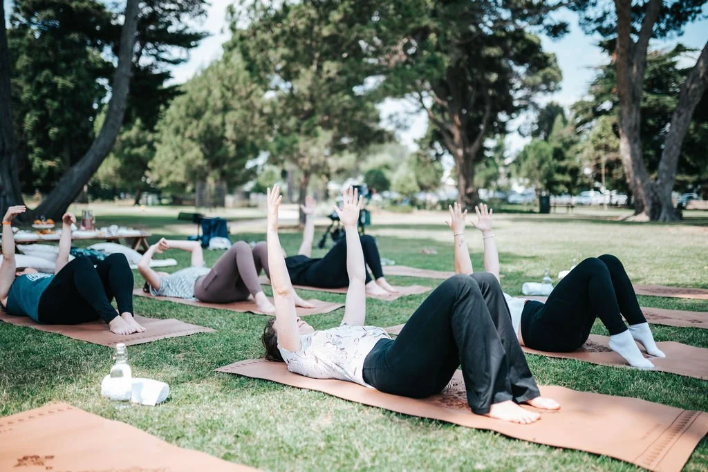 Guests participating in an outdoor Pilates session on premium mats in a scenic park setting.