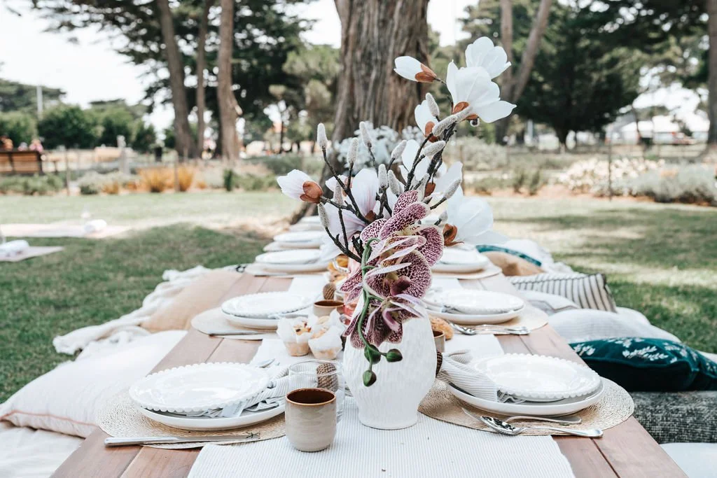 Beautifully styled outdoor picnic setting featuring premium tableware, elegant floral arrangements, and thoughtfully designed details in a scenic park location.