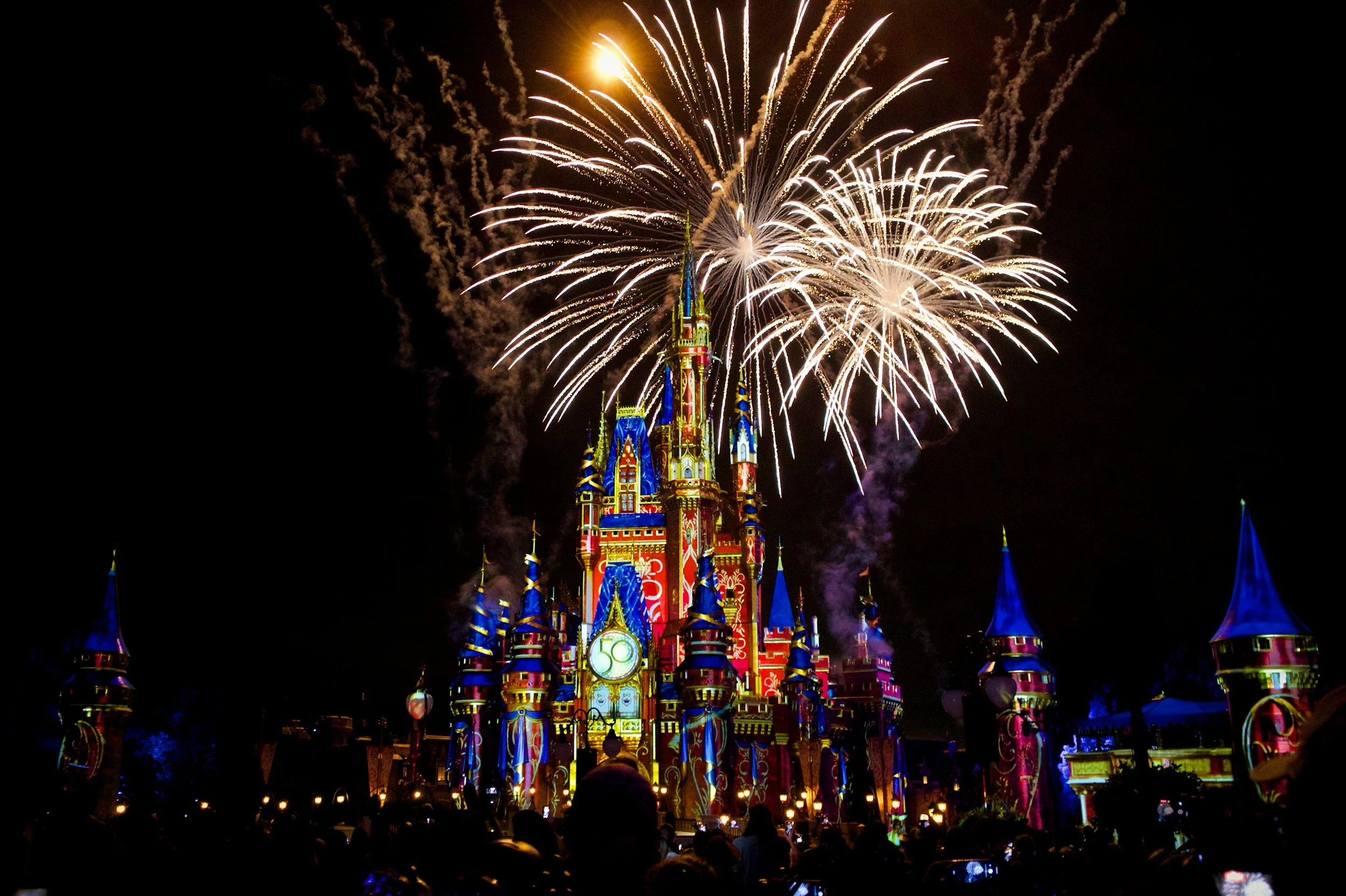 Fireworks exploding over a colorful Disney castle at night during a celebration.