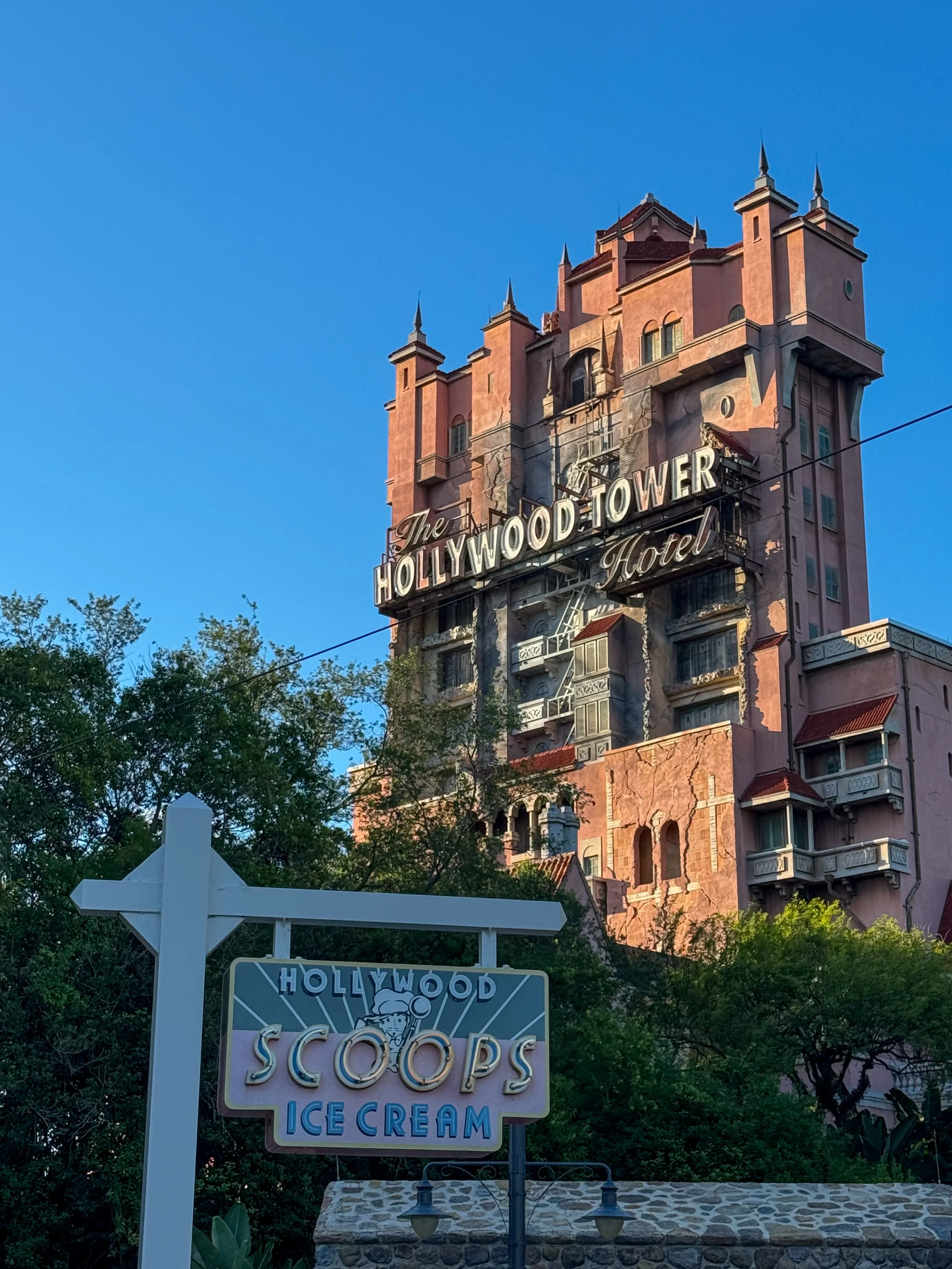 The Hollywood Tower Hotel, a tall pink building with gothic architectural features and a large sign that says "The Hollywood Tower Hotel," with a secondary sign in front advertising "Hollywood Scoops Ice Cream."