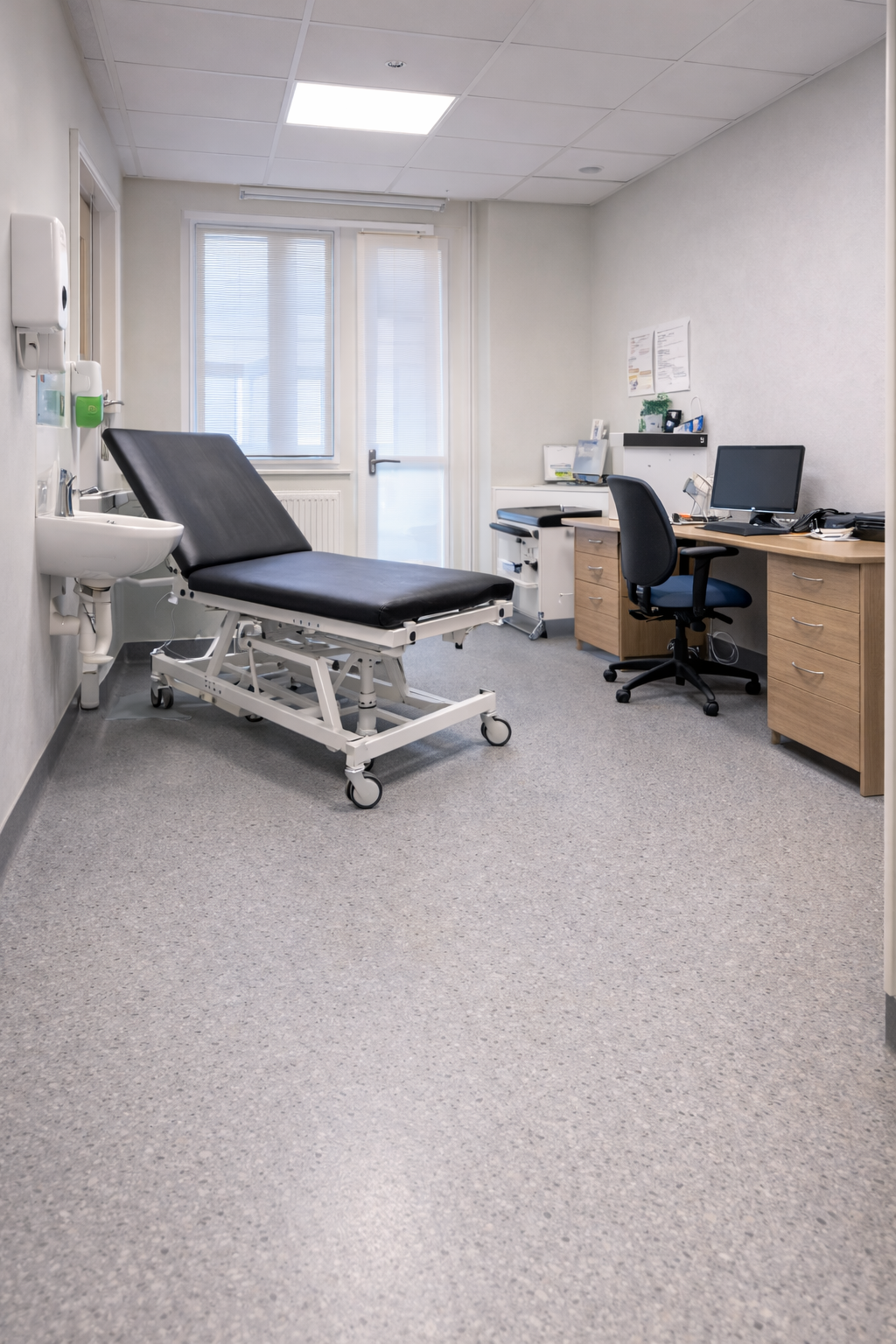 Commercial vinyl safety flooring installed in a UK GP surgery treatment room with desk computer chair and examination bed