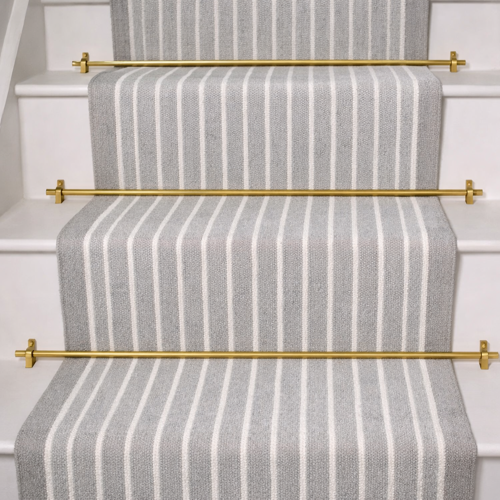 Light grey striped carpet stair runner with brushed brass stair rods in a luxury home staircase