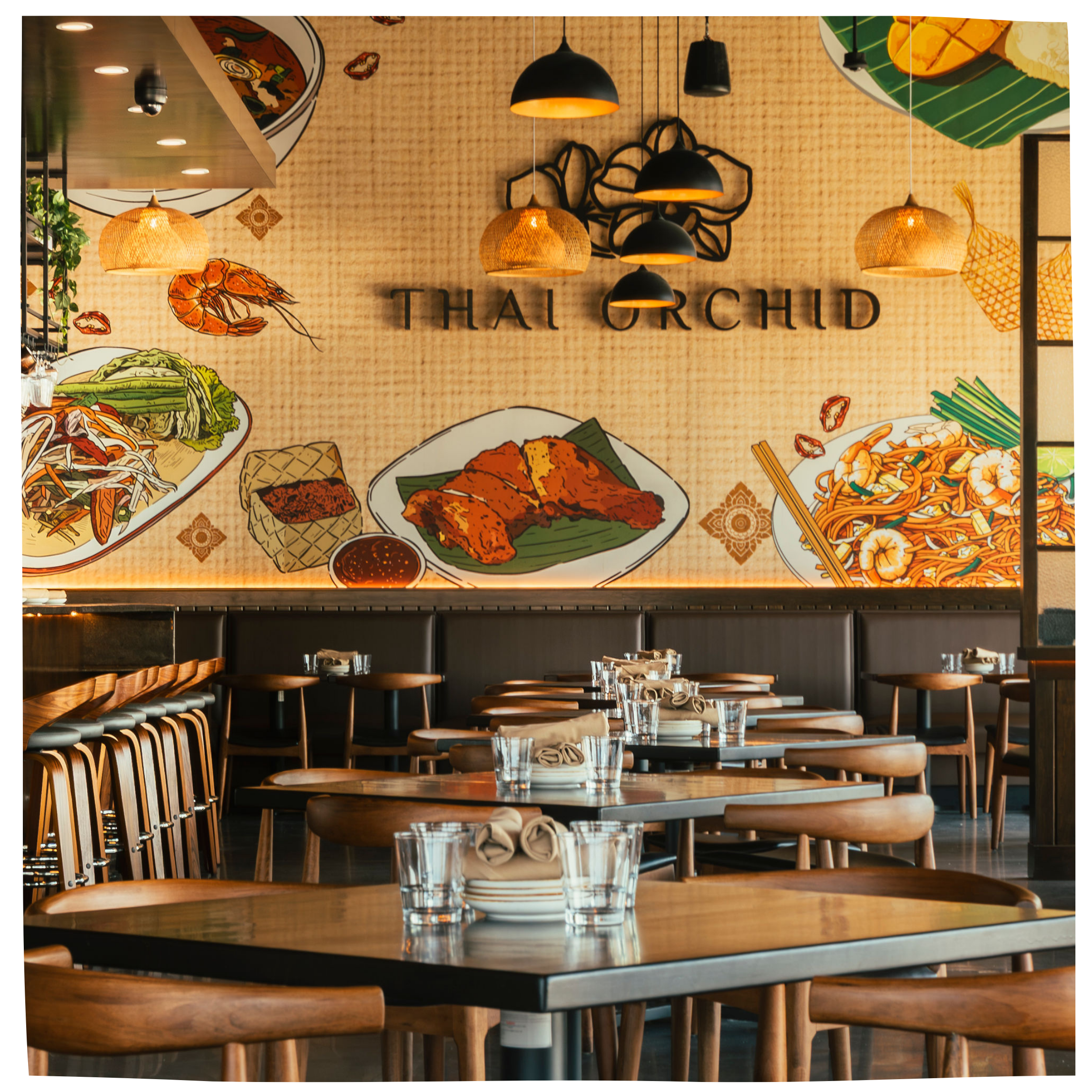 Empty Thai restaurant with wooden tables, napkins, and glasses, featuring a large wall mural of Thai dishes and the text 'Thai Orchid' in the background.