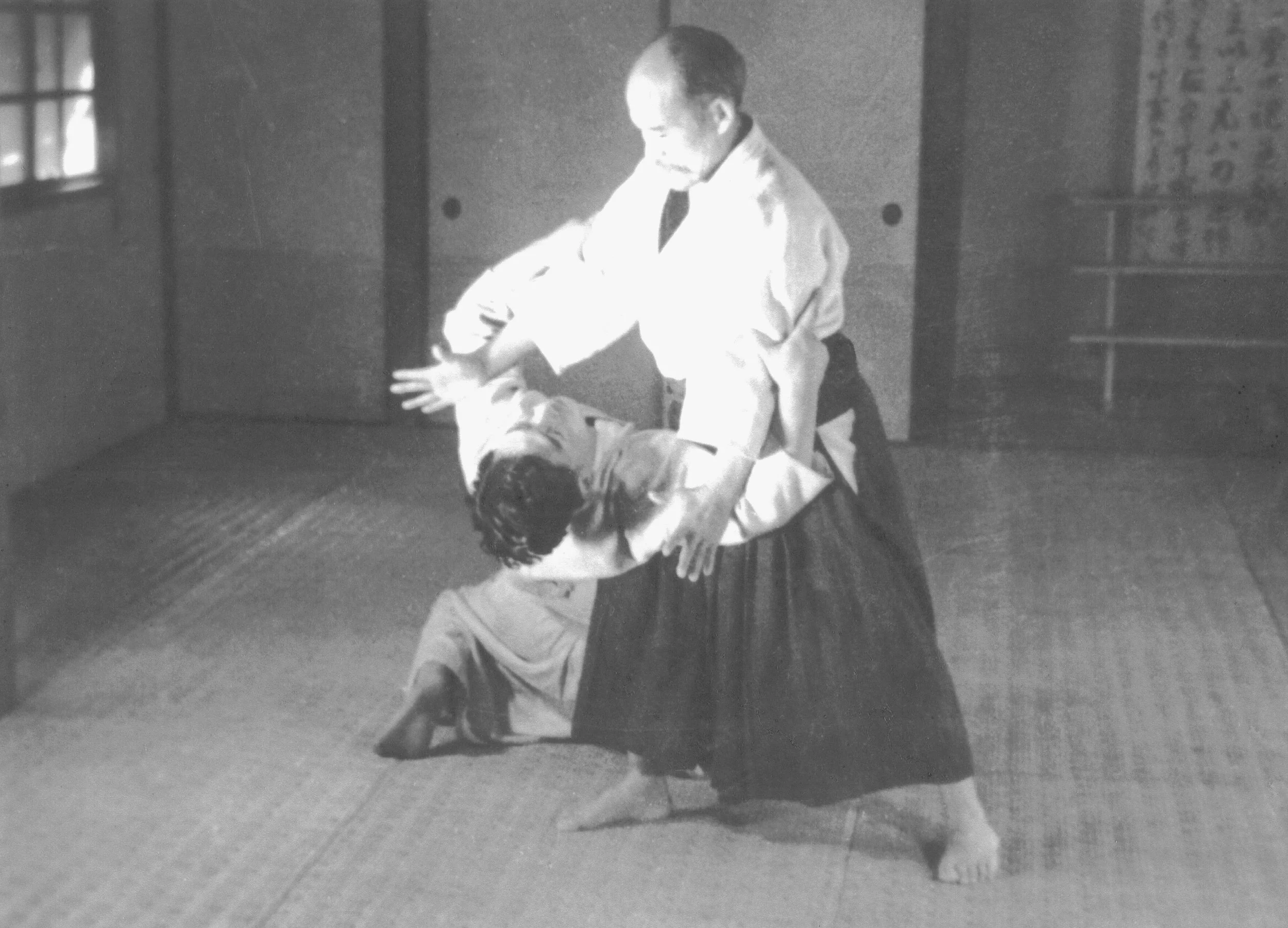 Two martial artists practicing judo in a dojo, with one person executing a throw on the other.