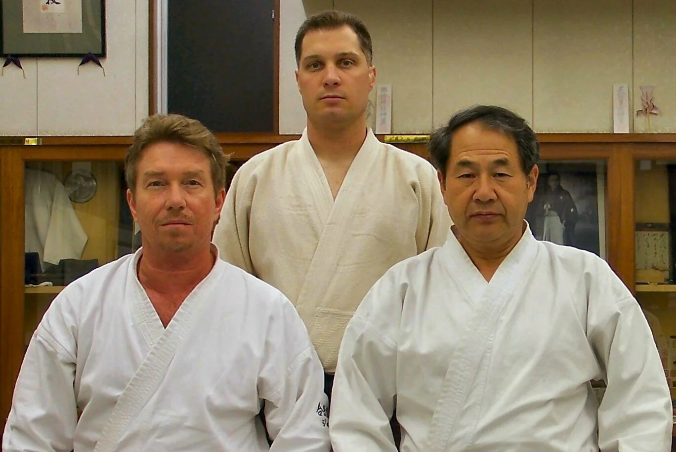 Three men dressed in karate gi uniforms posing in a martial arts dojo.