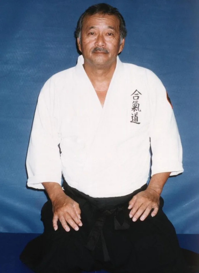 Man in white martial arts gi sitting on blue mat, with Japanese characters on the gi