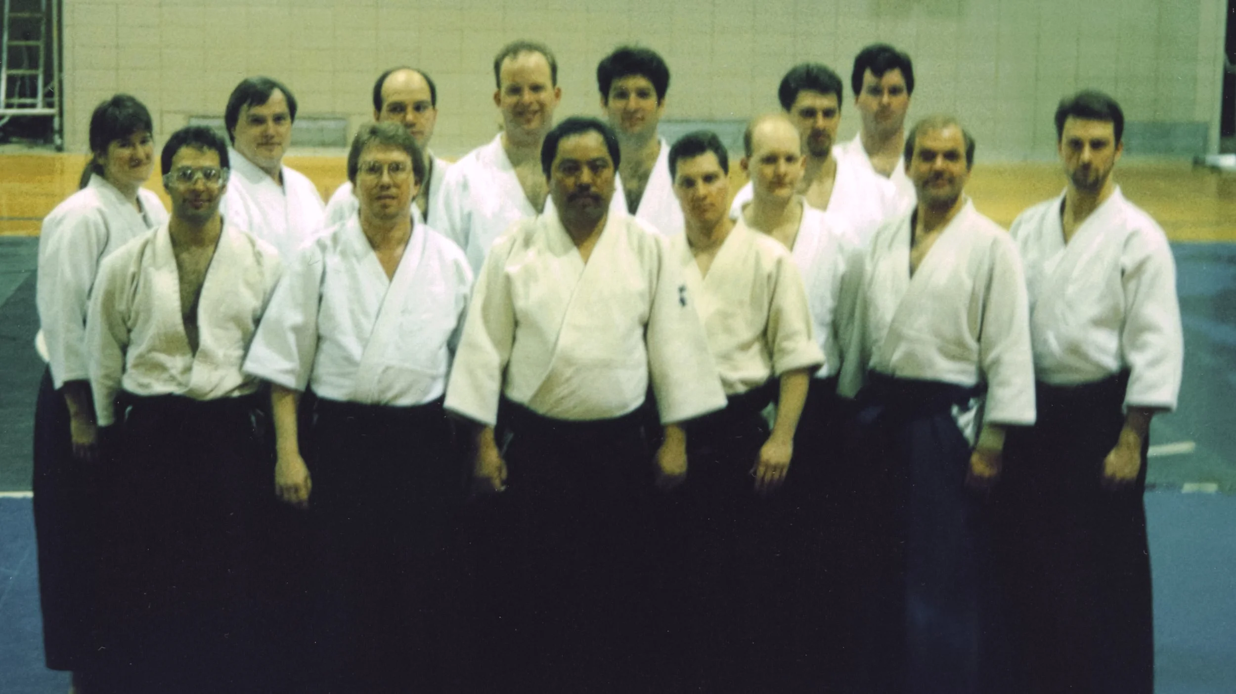 A group of men and women in martial arts uniforms standing together in a gymnasium.