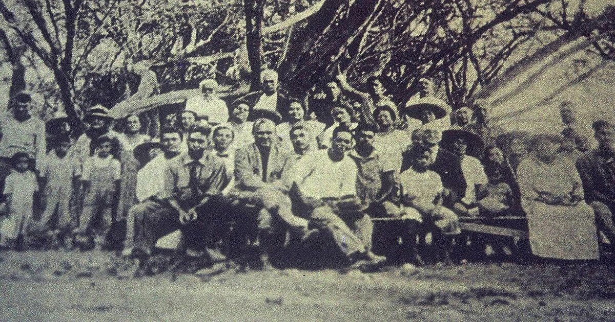 A vintage black-and-white photograph of the first Native Hawaiian homestead families posing together outdoors beneath kiawe trees at the Kalanianaʻole Settlement in Kalamaʻula, Molokaʻi, circa 1923.