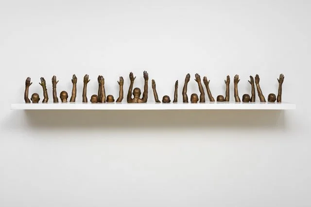 A bronze sculpture  several figures with raised hands by Willis Thomas, entitled "Raise Up", made in 2013.  Measuring 112 x 10 x 4 in.; Viewable at the Jack Shainman Gallery, New York, and Goodman Gallery, South Africa.