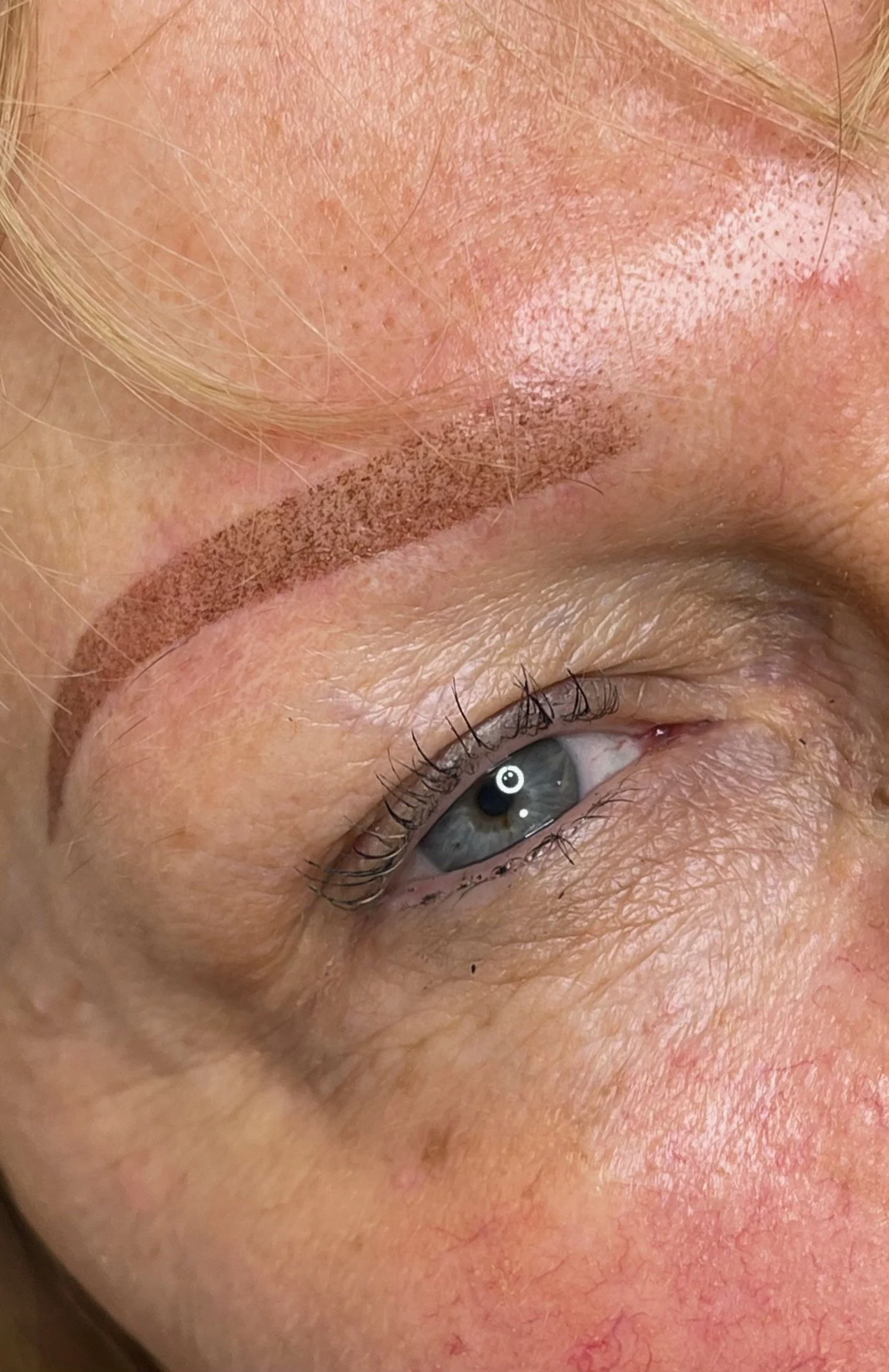 Close-up of a person's eye with makeup and a cosmetic tattooed eyebrow.