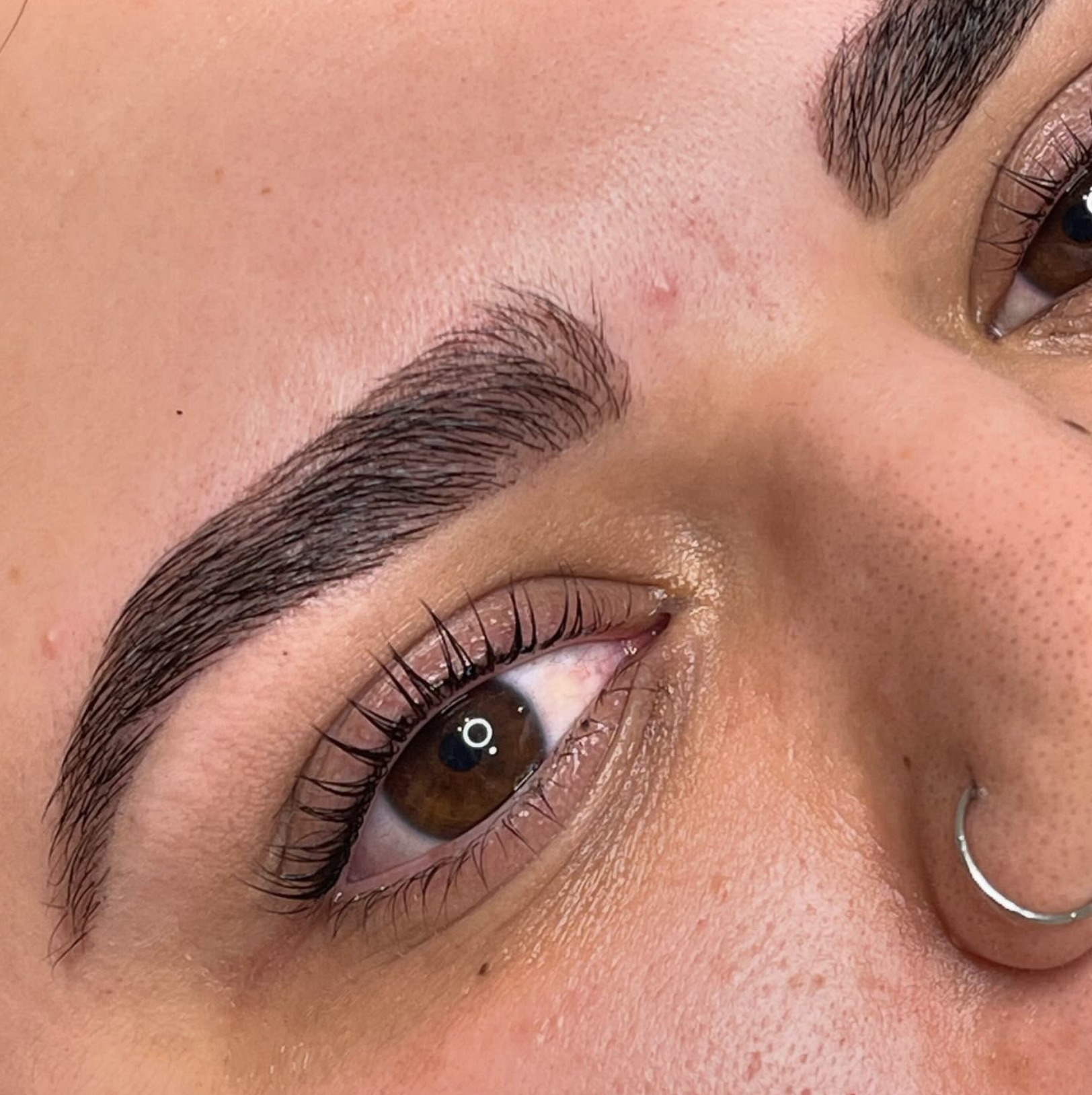 Close-up of a person's eye with long eyelashes, well-defined eyebrows, and clear skin, showing detailed skin texture and makeup.
