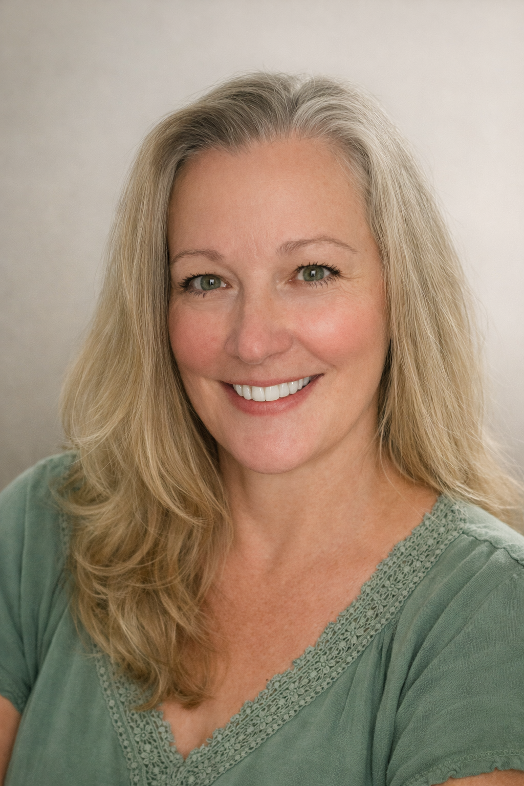 A close-up portrait of a woman with long, wavy blonde hair and green eyes, smiling, wearing a green top with lace detail.