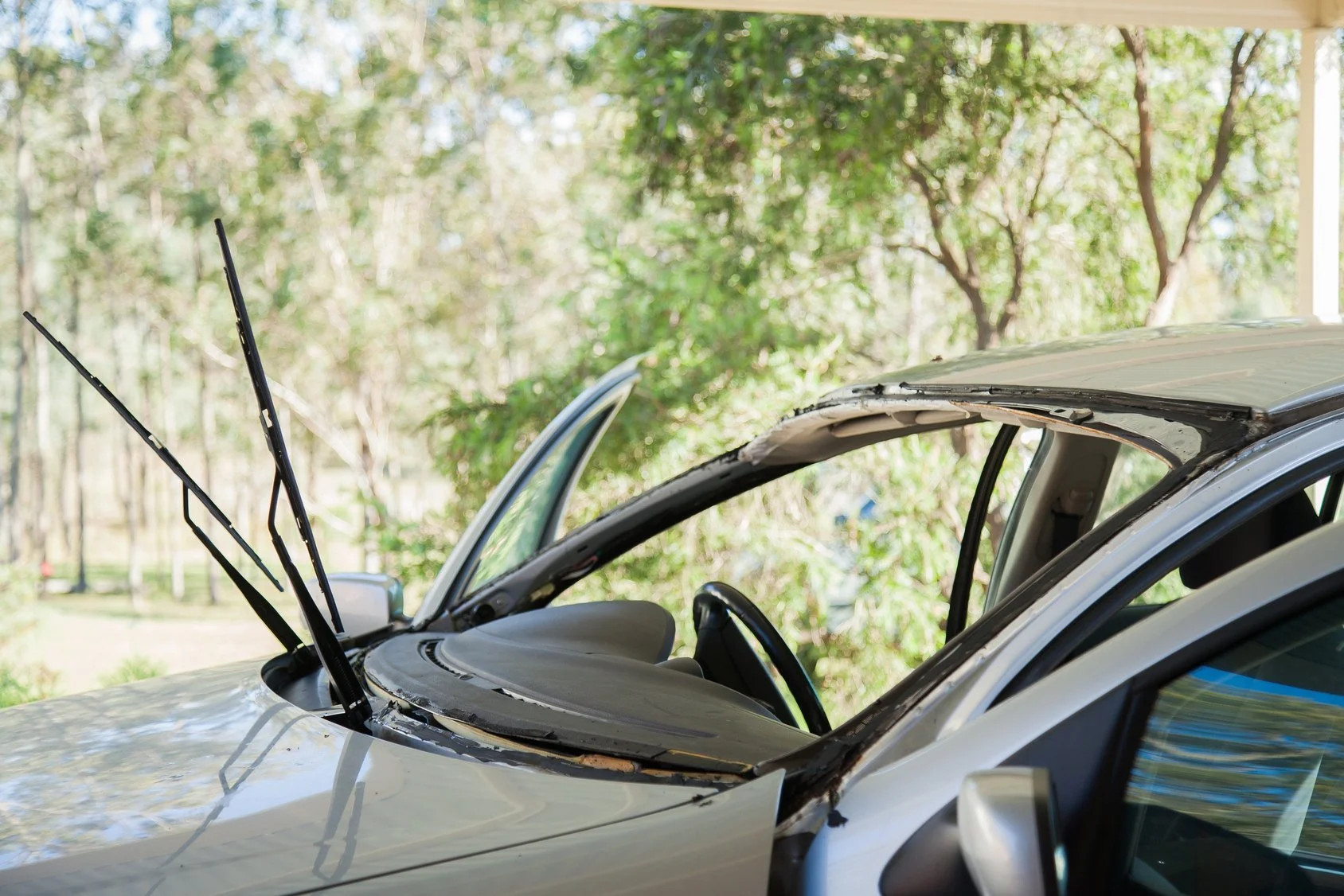 A windshield being replaced on a silver sedan in the middle of a park.