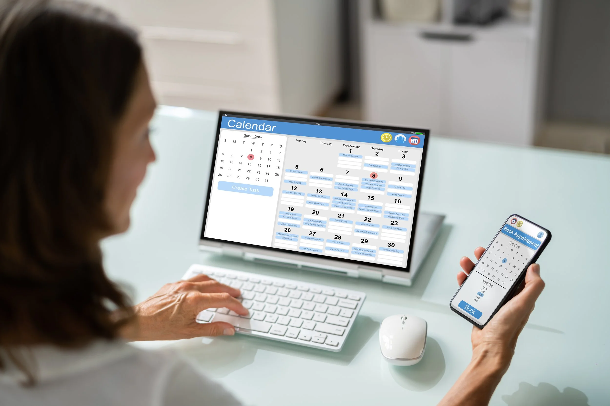 A woman uses a smartphone to book an appointment, with a digital calendar on her laptop screen showing scheduled tasks and appointments for the month.