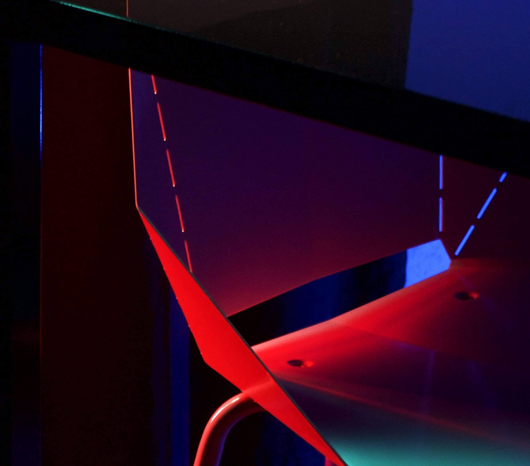 An angular chair bathed in hot red light with slivers of contrasting teal against a dark backdrop. Surreal color study.