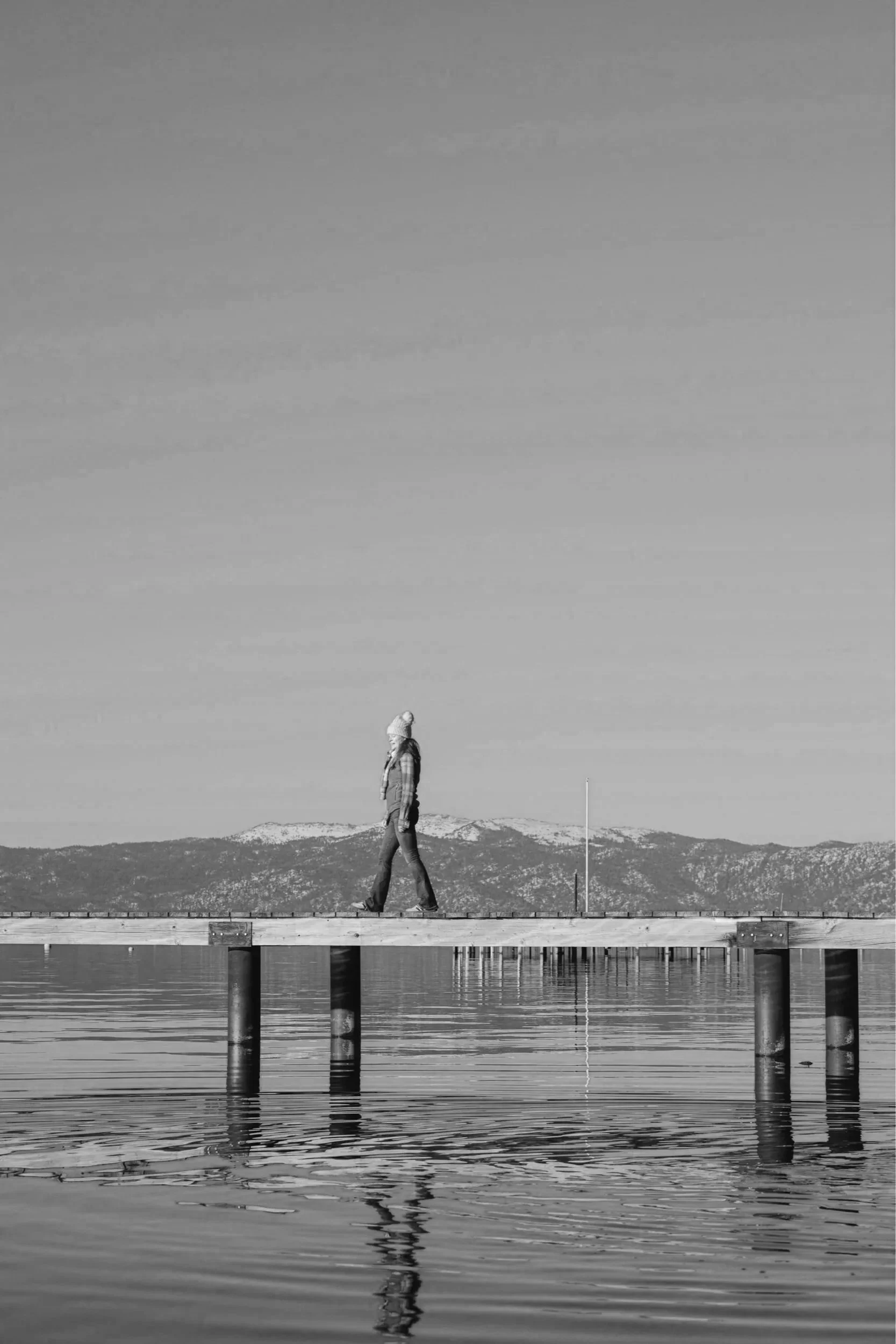 Woman walking along a wooden dock over a calm Lake Tahoe with mountains in the distance